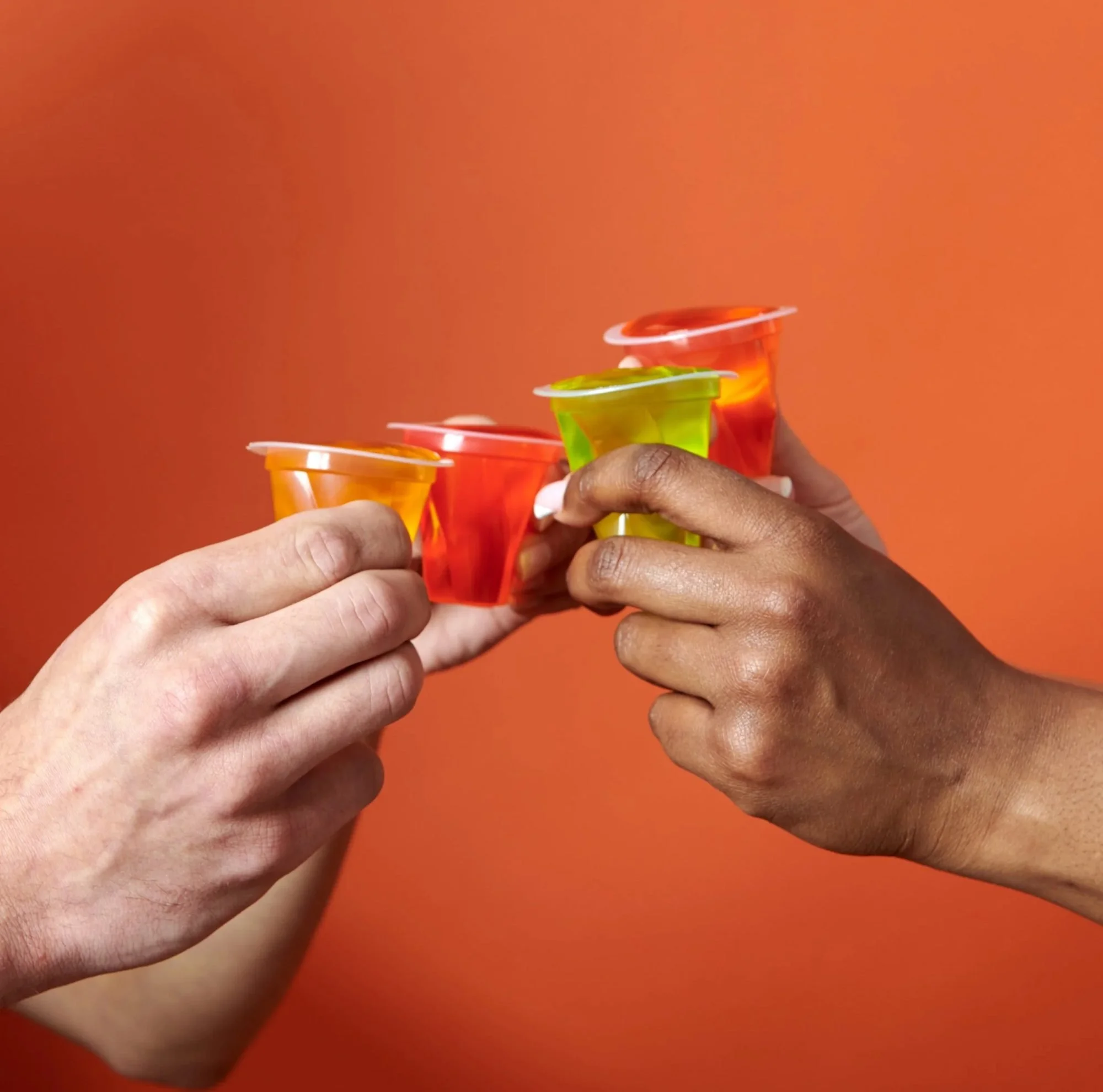 Hands toasting colorful jelly cups on orange, CPG snack lifestyle photography