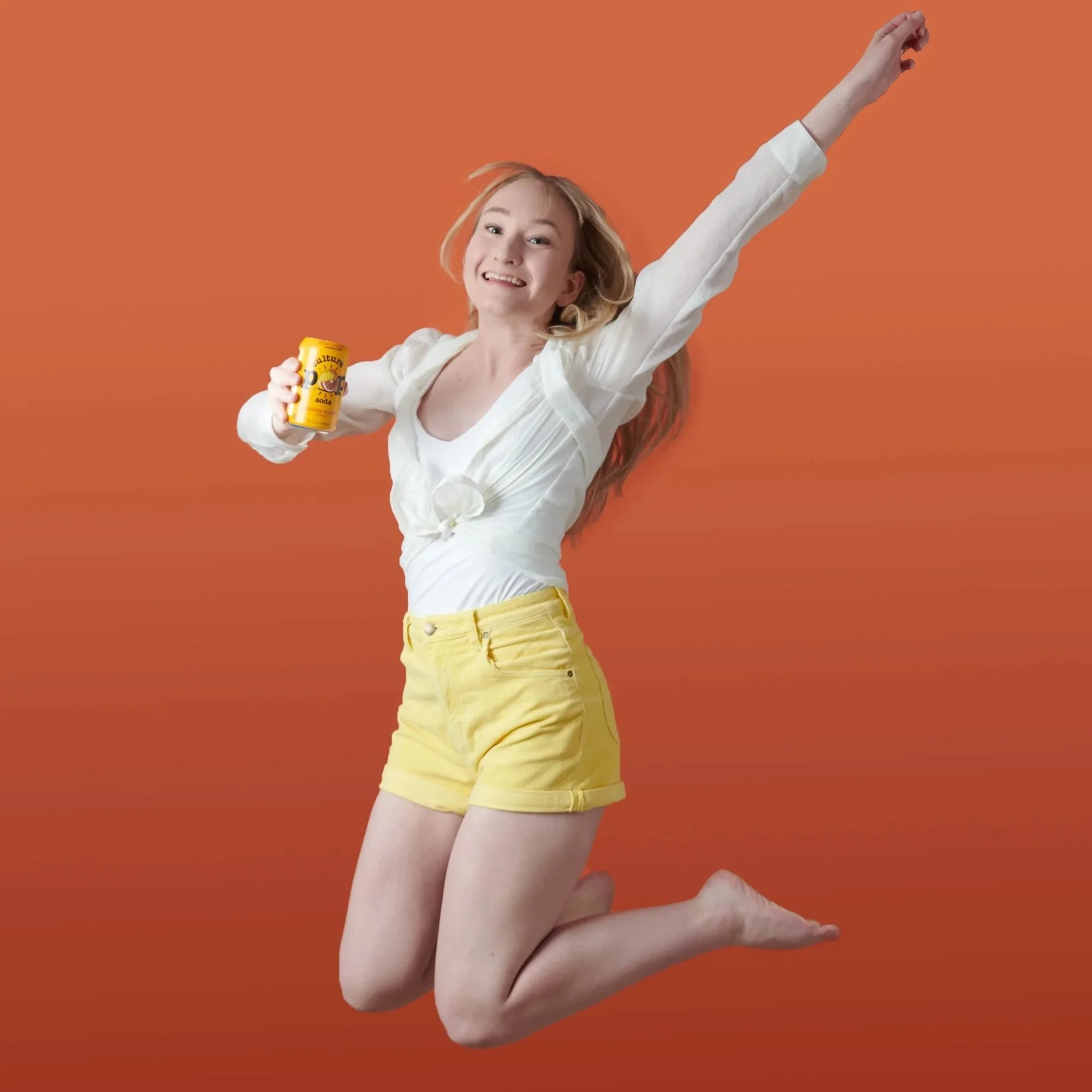 Model jumping with joy holding a product on orange, CPG lifestyle photography
