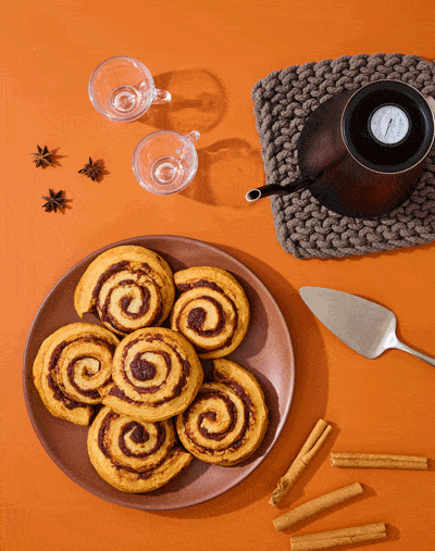 Hand icing cinnamon rolls with coffee and spices on orange, food stop motion
