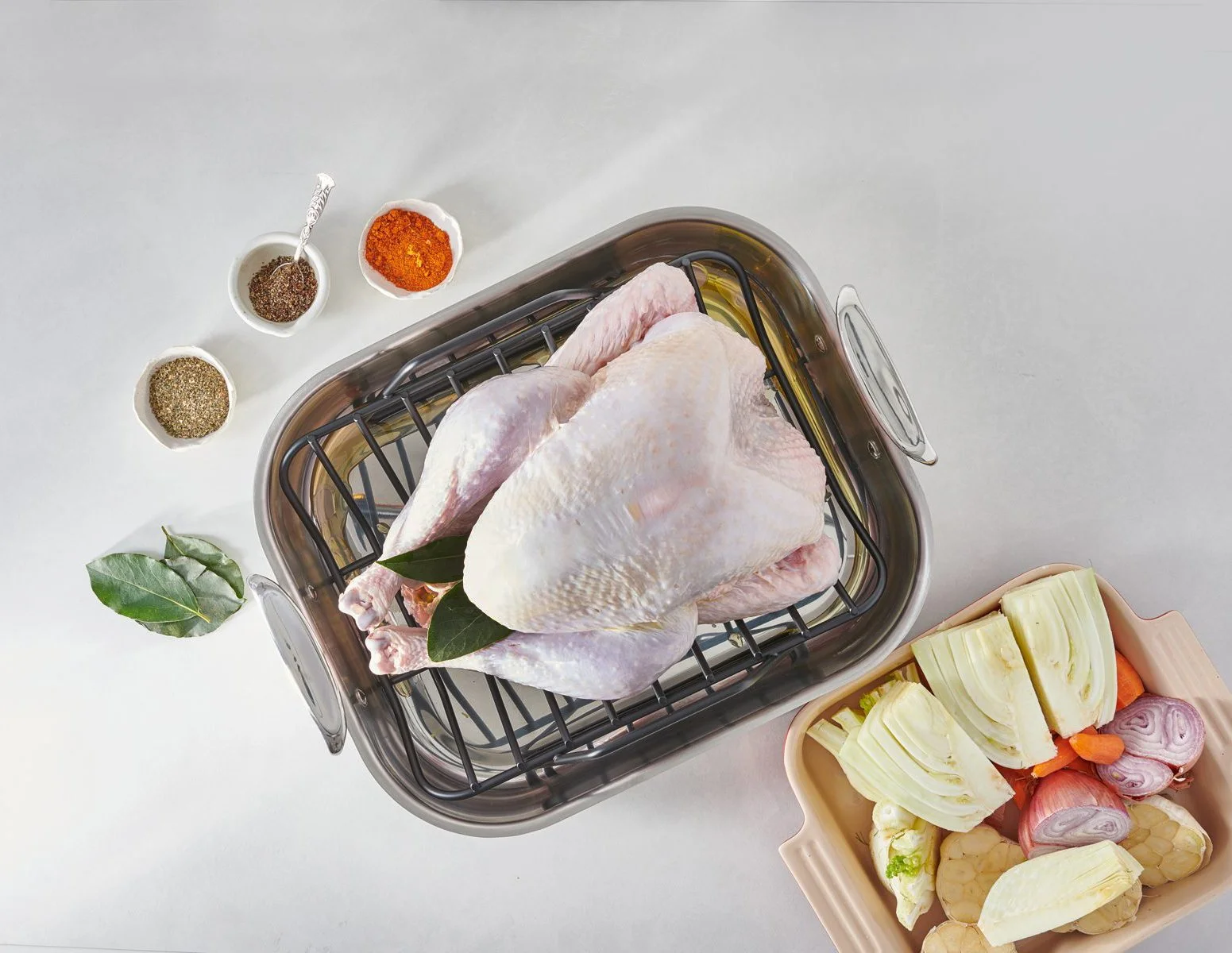 Raw turkey in a roasting pan with prep ingredients. Process photography for holiday recipes.