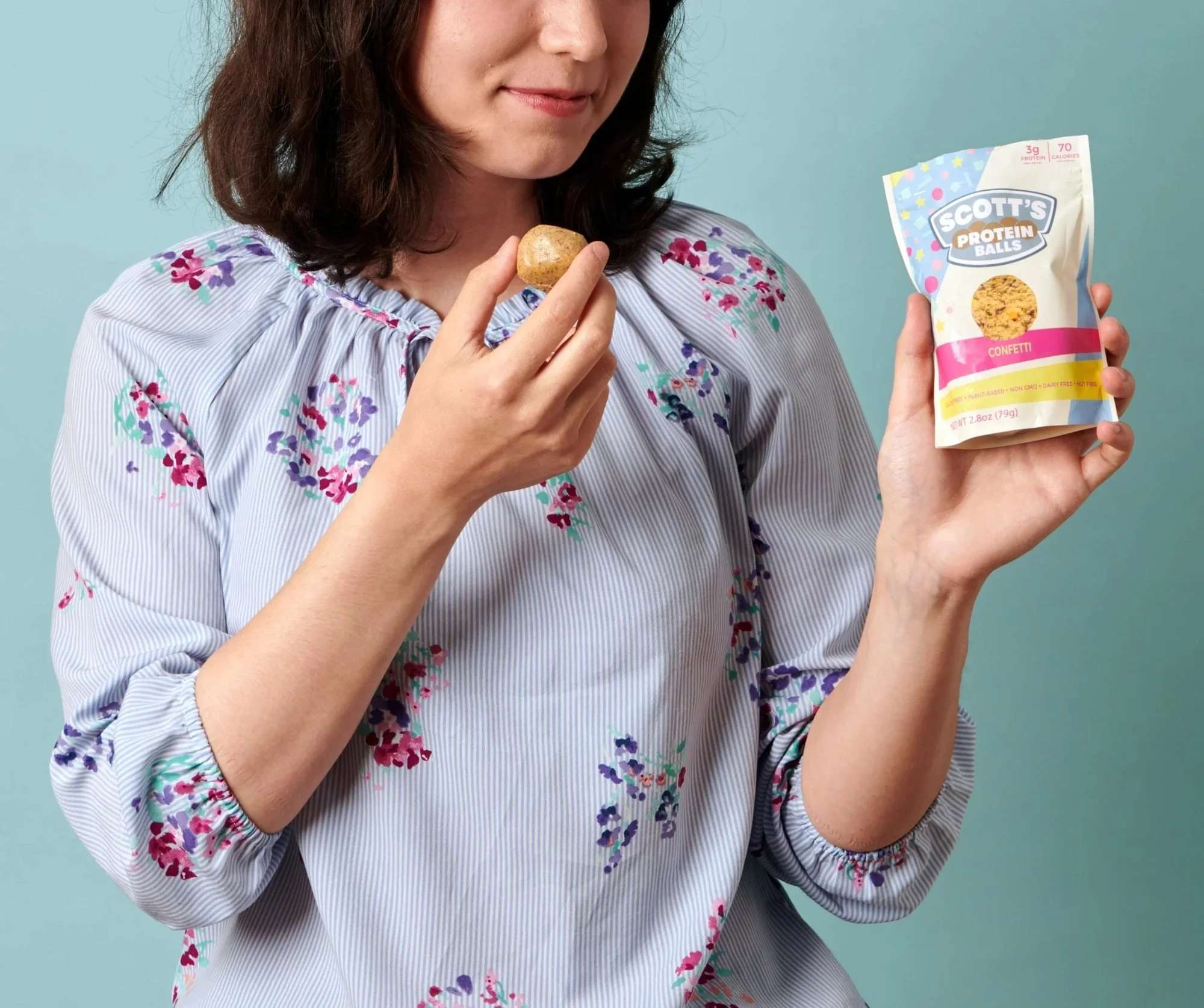Woman eating a protein ball holding a snack bag on blue, CPG snack lifestyle photography