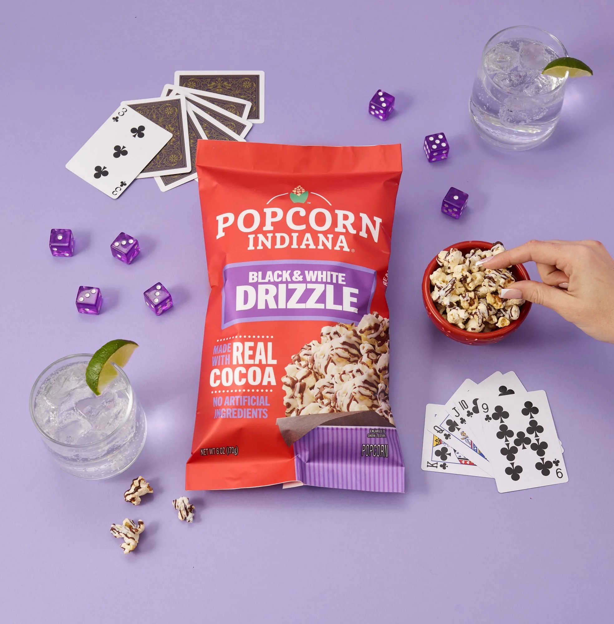 Popcorn Indiana Black and White Drizzle bag with cards, dice and drinks on purple, CPG snack photography