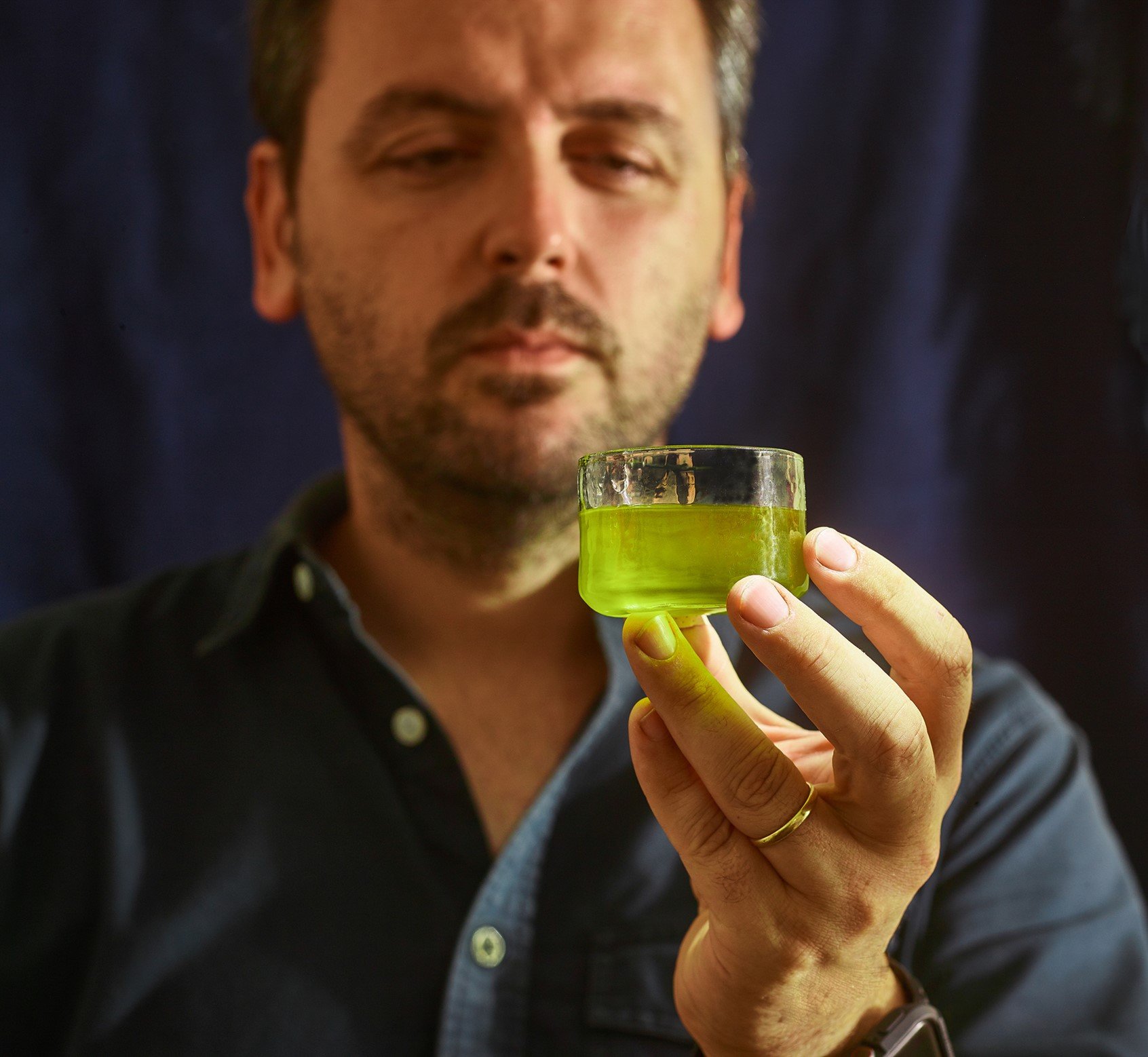 Olive oil maker tasting fresh green olio nuovo from a glass at the mill, editorial food photography by Judy Doherty