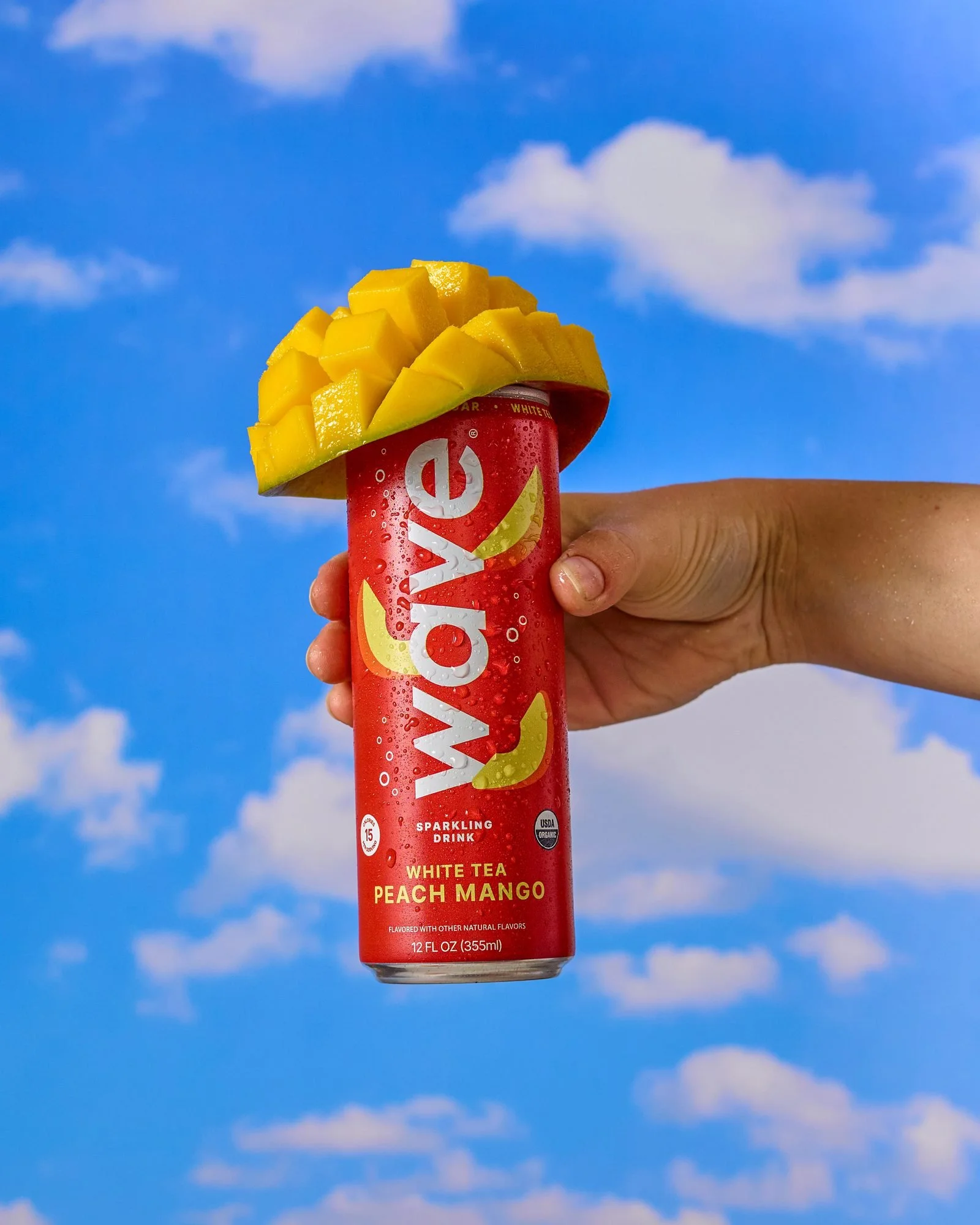 Hand holding a Wave white tea peach mango sparkling can against a blue sky, CPG beverage photography