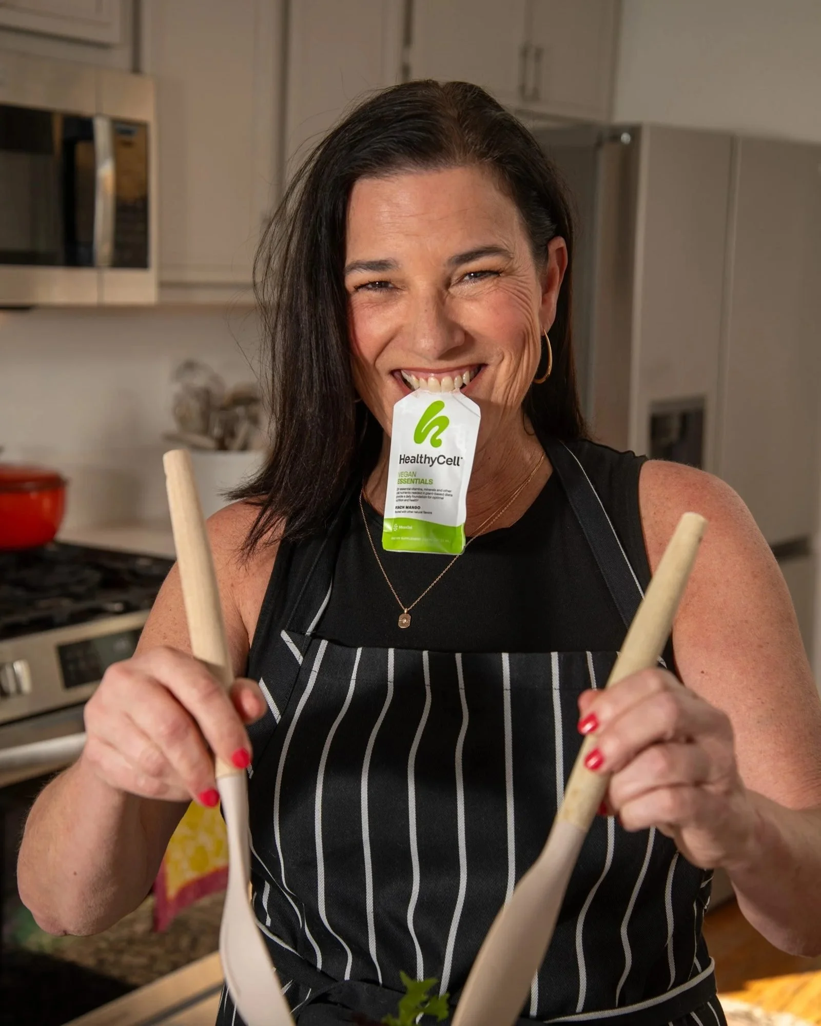 Woman in an apron holding wooden spoons with a supplement pouch, CPG lifestyle photography