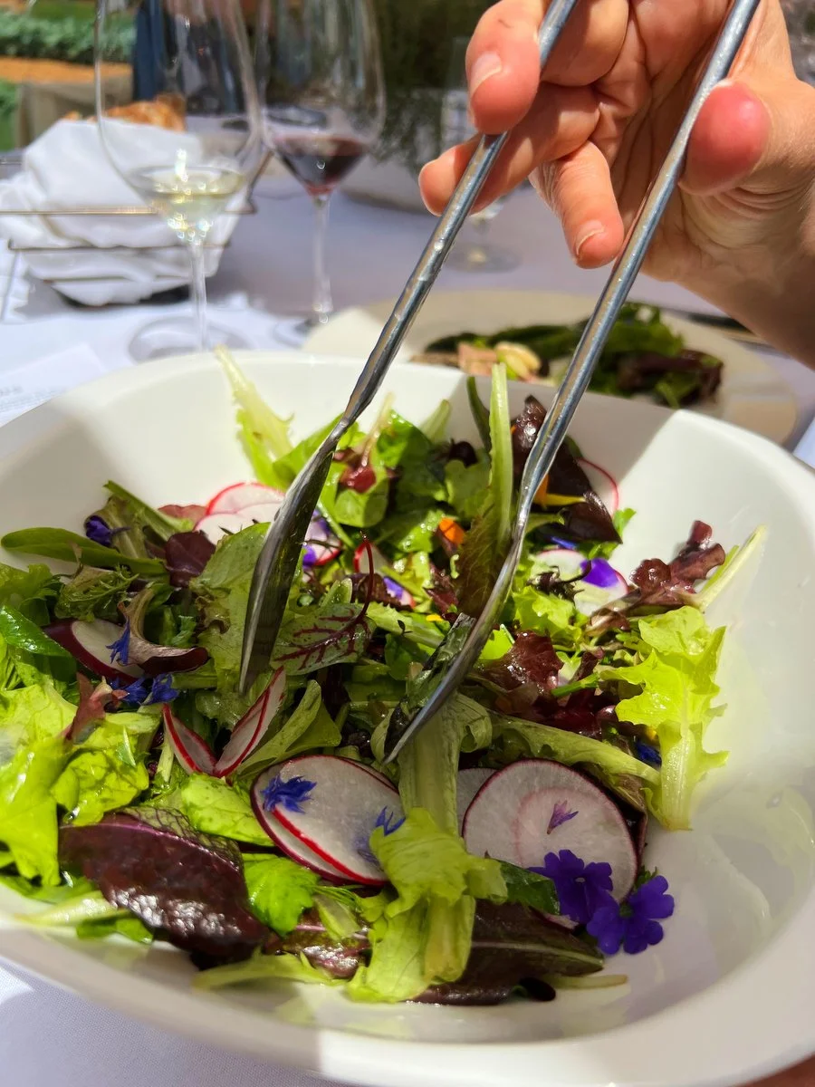 Salad being tossed with tongs and edible flowers