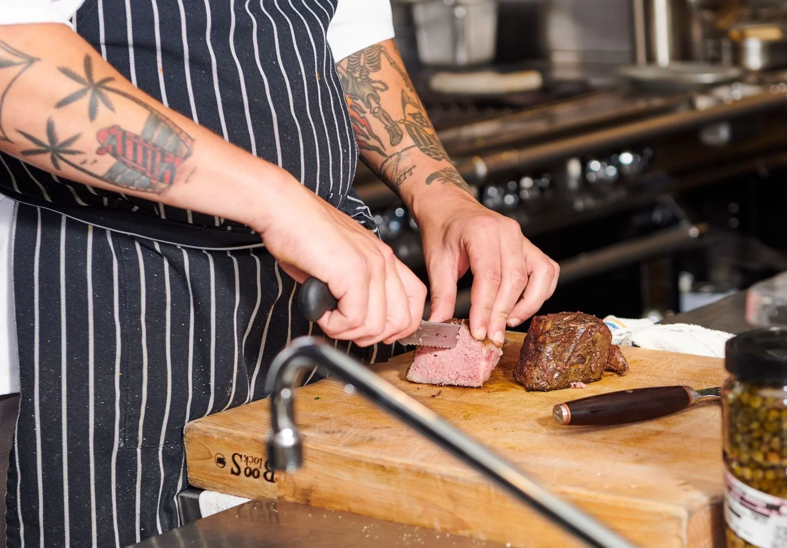 Chef with tattooed arms carving meat on a board