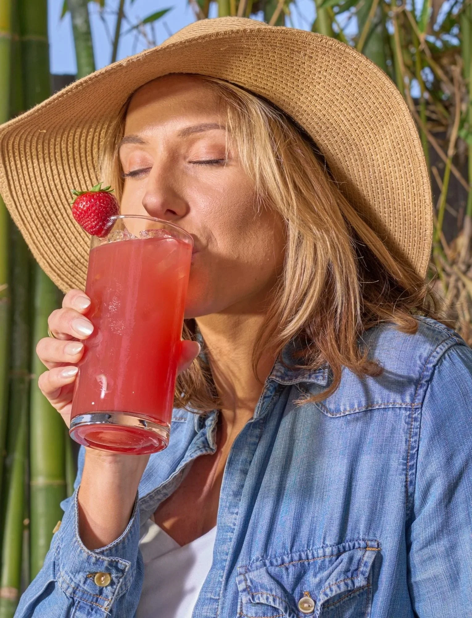 Woman in a straw hat sipping a pink drink, beverage lifestyle photography