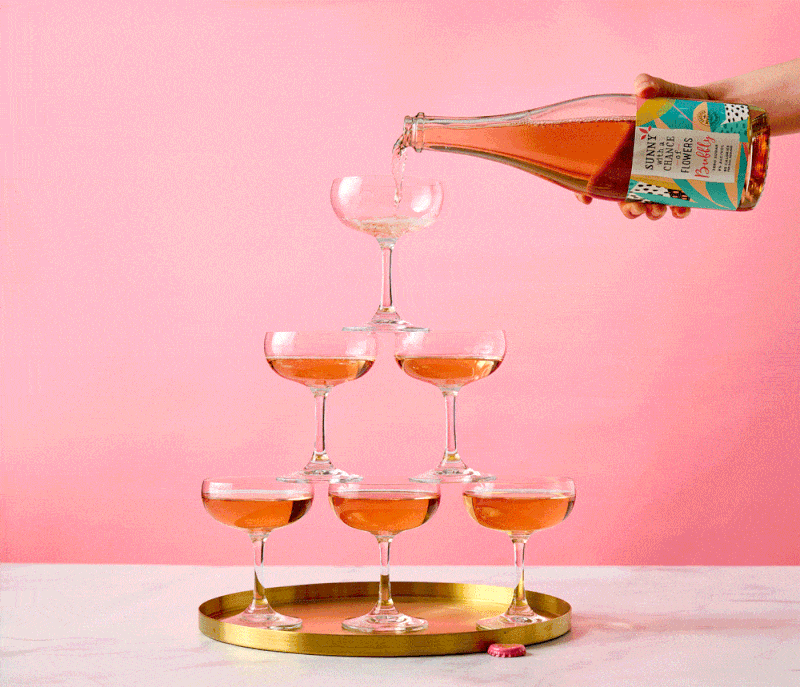 Sparkling wine poured over a coupe glass tower on pink, beverage stop motion
