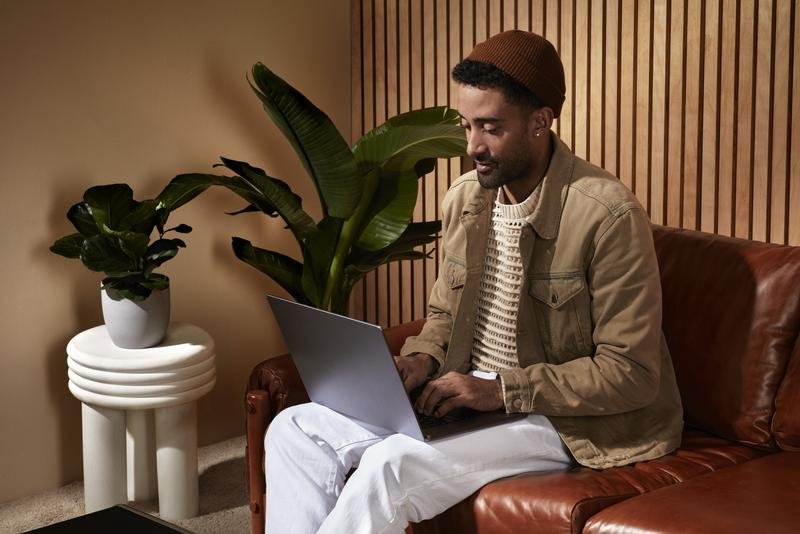 A man sitting on a leather couch looking at a laptop