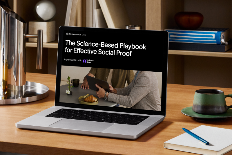 The Science-Based Playbook for Effective Social Proof displayed on a laptop computer next to a notebook, pencil, and plated mug, all seated on a table.