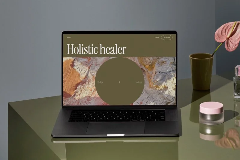 A laptop on a green desk showing a website for a holistic healer.