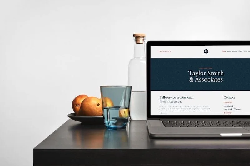 An open laptop, glass of water, and oranges in a bowl on a dark table