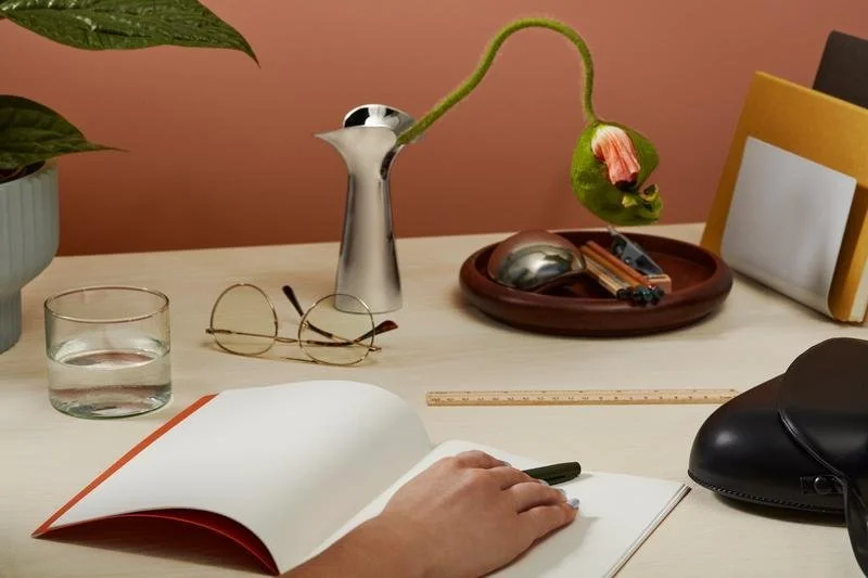 A hand resting on a notebook and surrounded with items on a desk