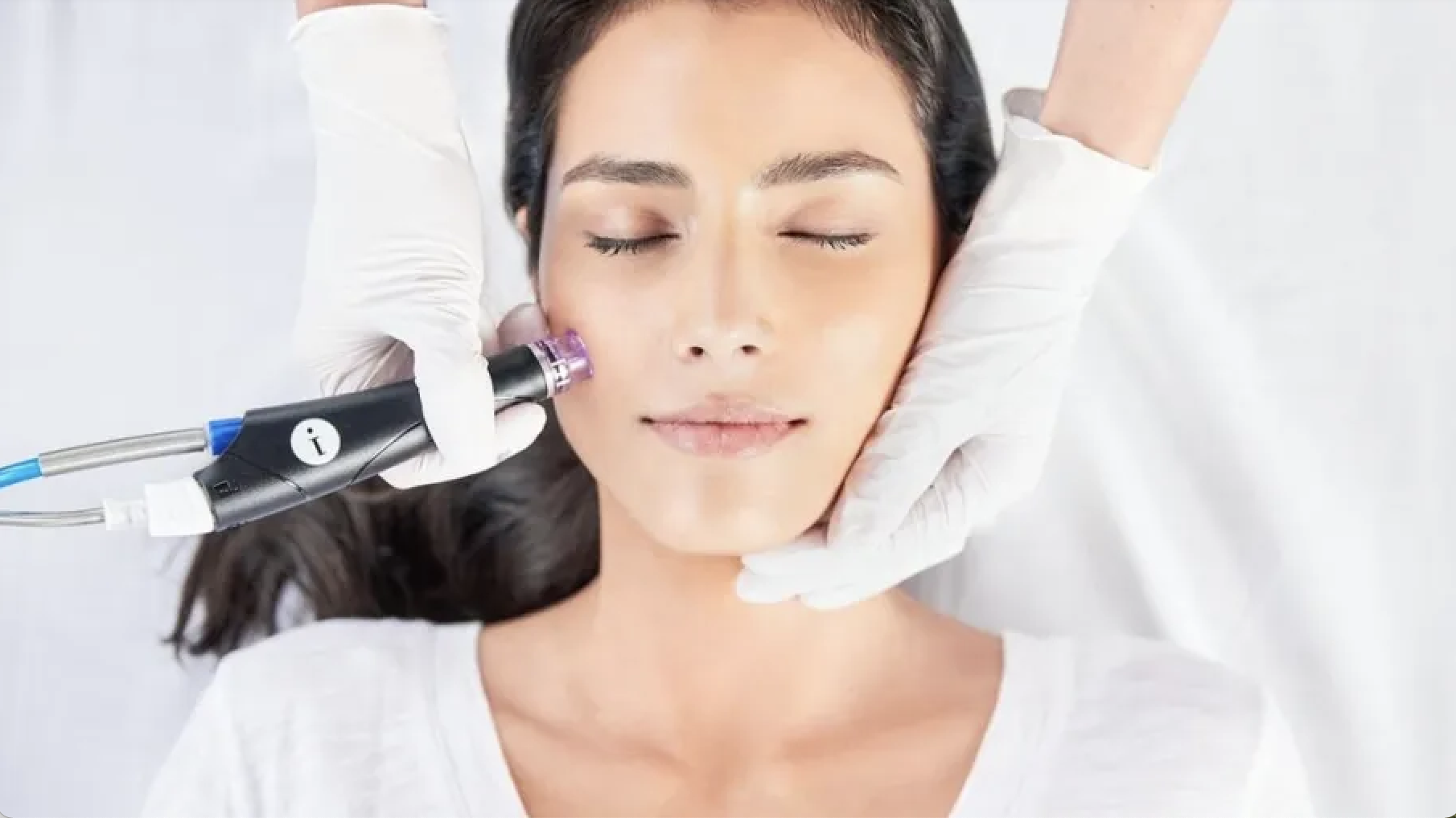 Person receiving a facial treatment with a cosmetic device operated by gloved hands.