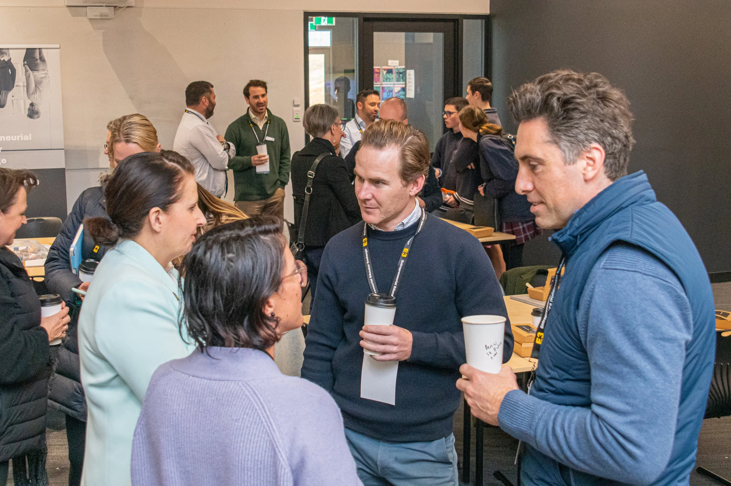 A group of people engaging in conversation at a professional event or conference, with some holding coffee cups.