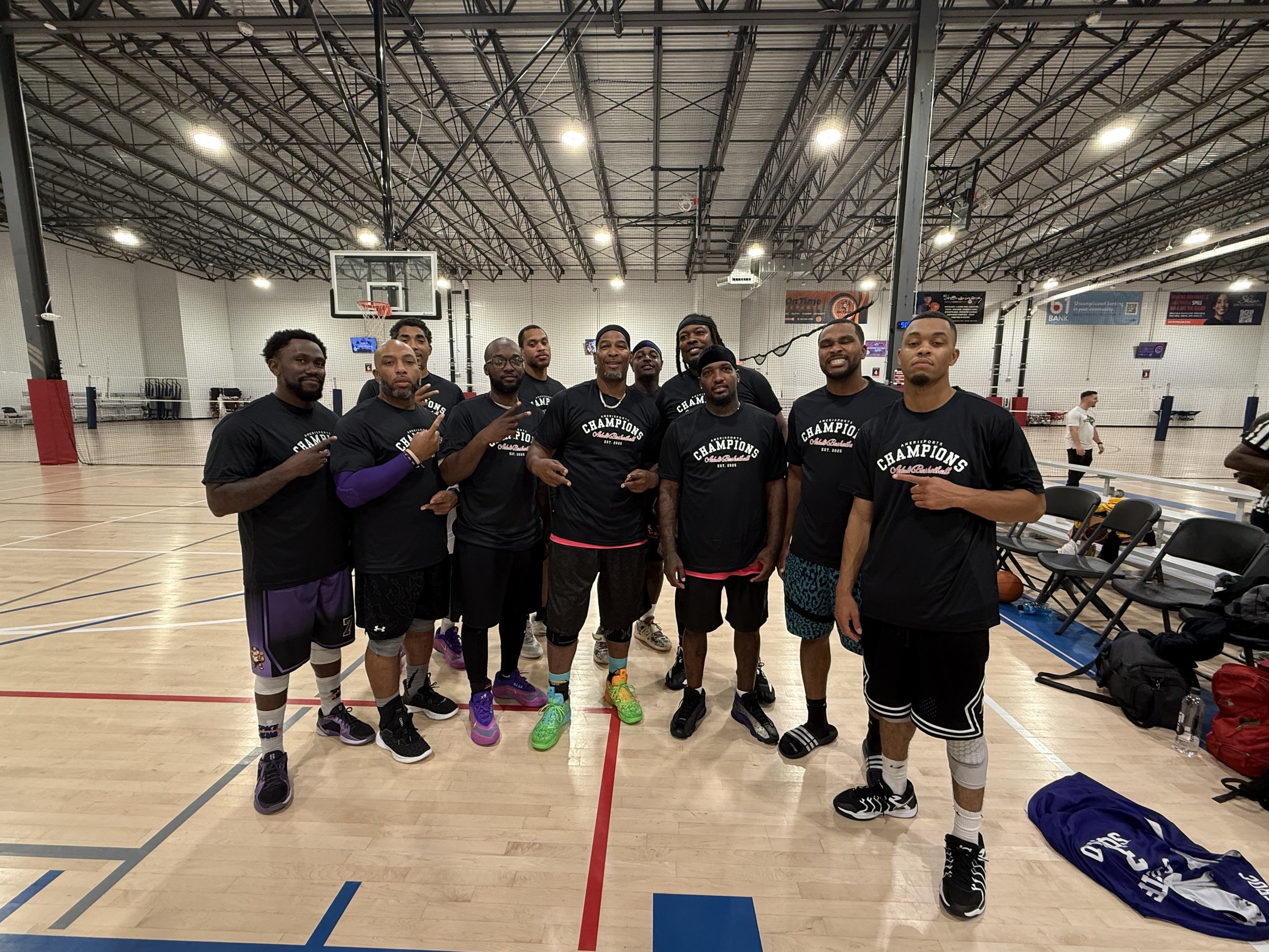 Group of men in black t-shirts standing inside an indoor basketball court, posing for a photo.