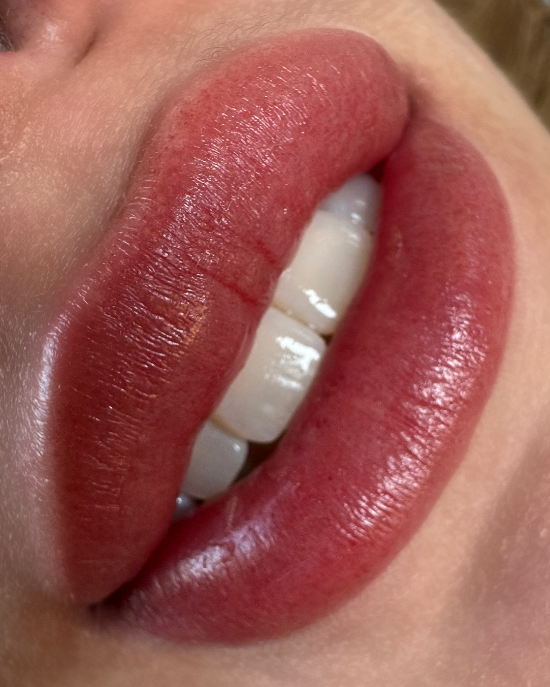 Close-up of lips with red lipstick, showing teeth partially visible.