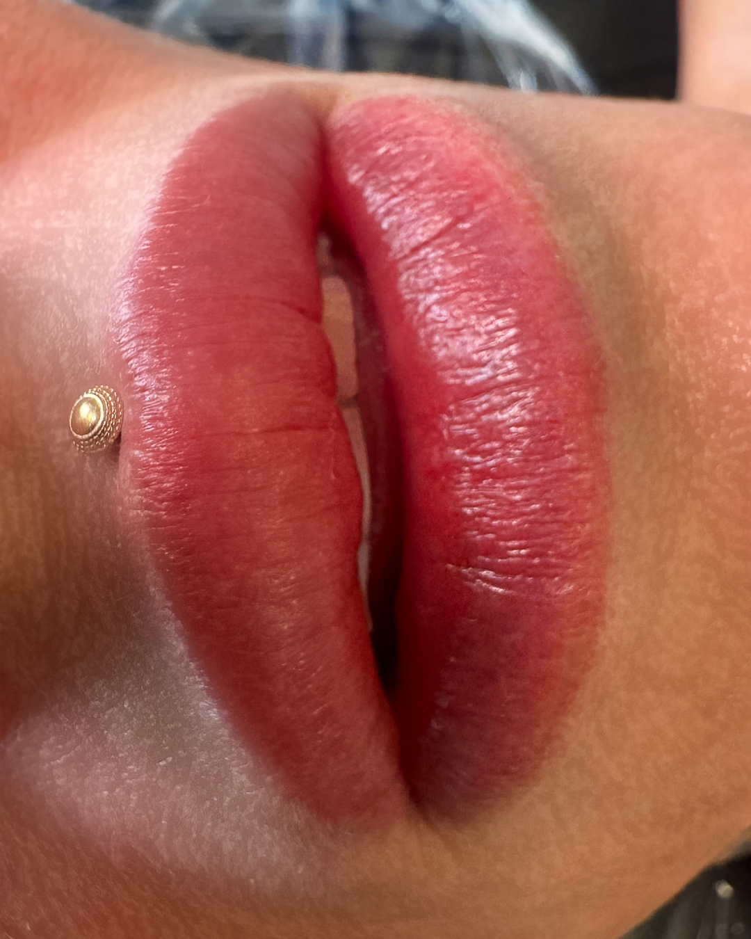 Close-up of lips with lip gloss and a small nose piercing.