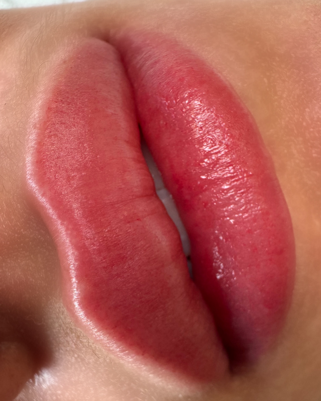 Close-up of slightly parted lips with natural skin tone, showing full, pink lips with a glossy finish.