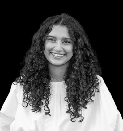 Black and white photo of a young woman with curly hair smiling, wearing a light-colored top against a dark background.