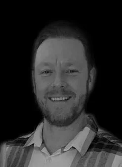 A smiling man with a beard in a plaid shirt