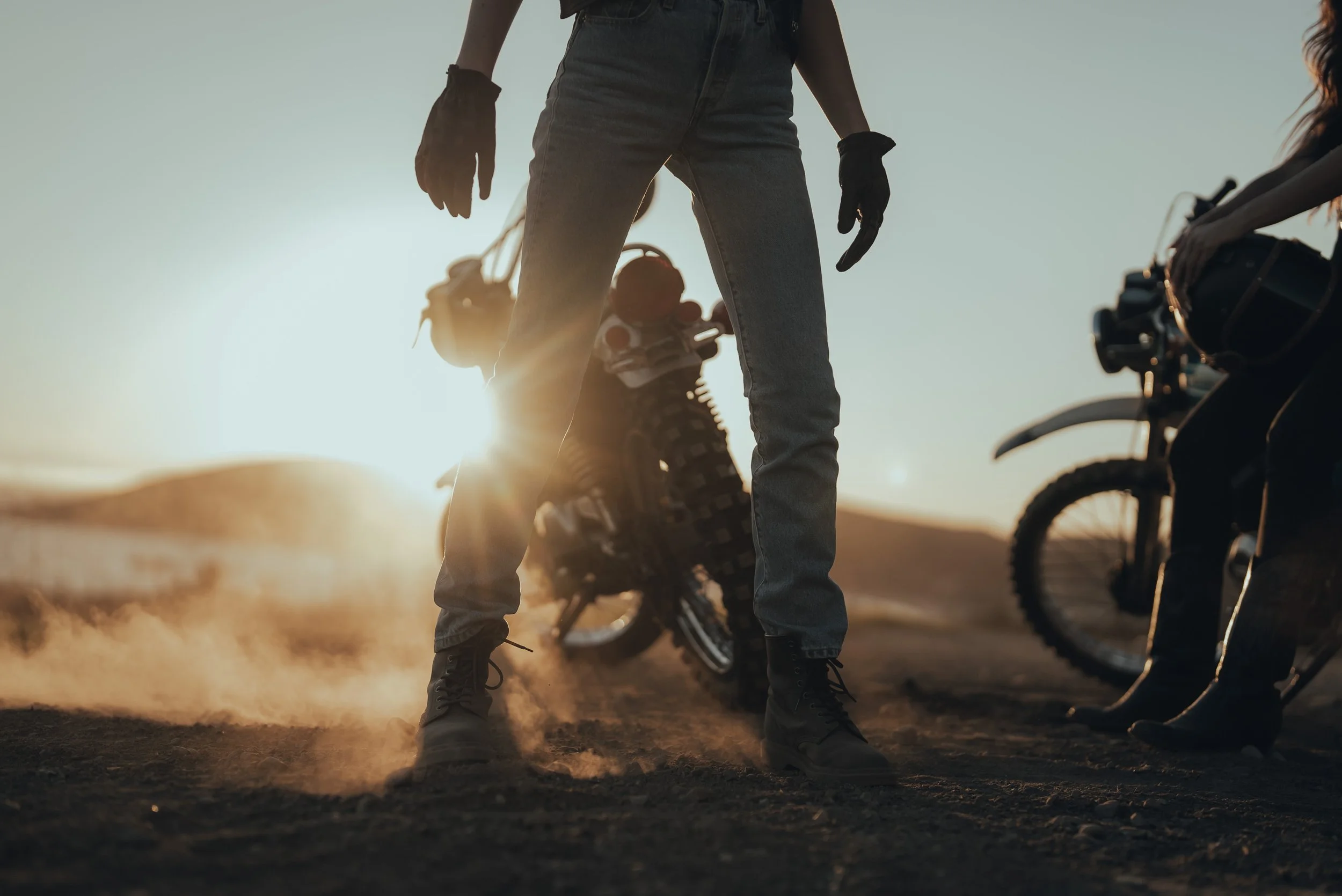 Silhouettes of people with bikes in a desert, with the setting sun in the background.