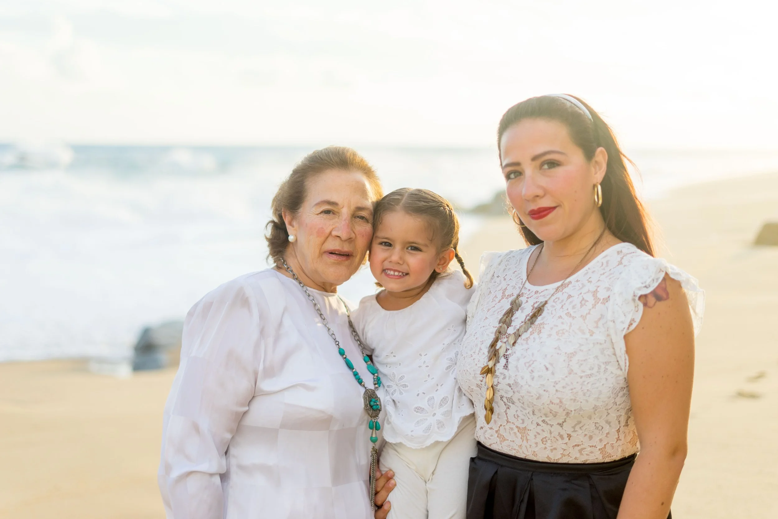 Three women and a young girl standing on a beach at sunset