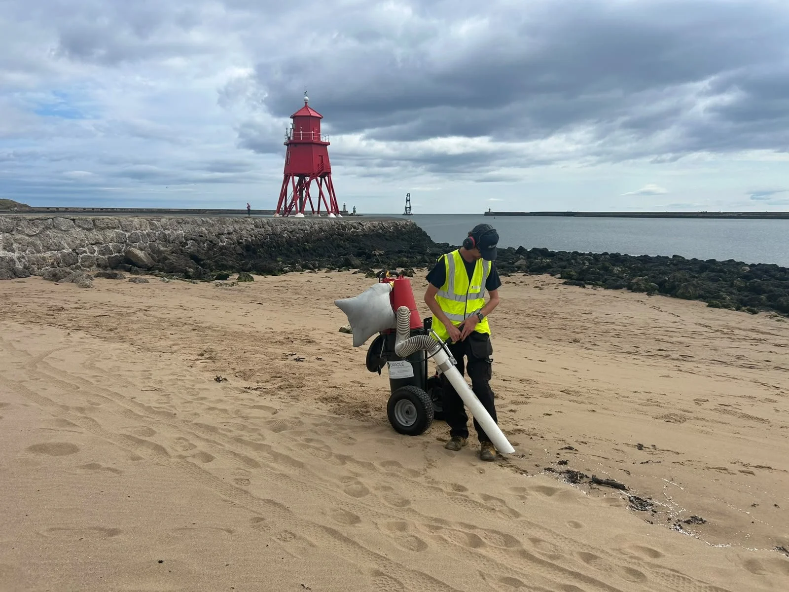 Image of OEE staff member using a vacuum cleaner sucking up nurdles from the shoreline.