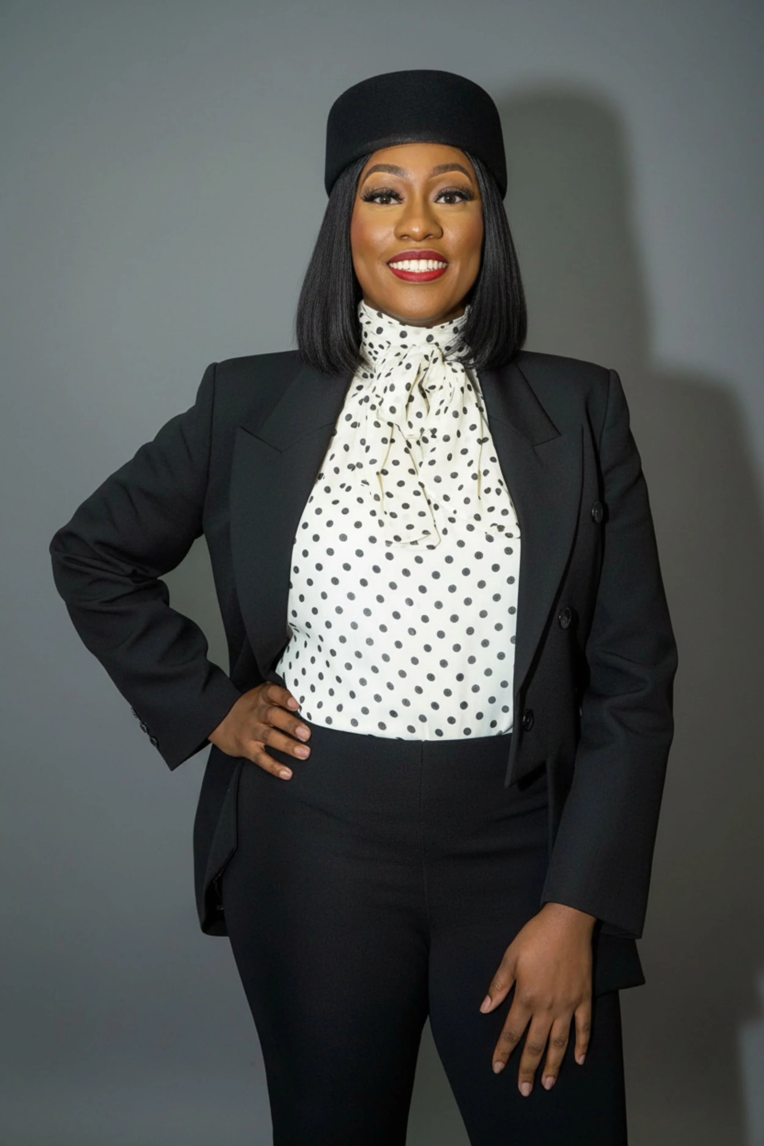 Akua Barnie with straight, shoulder-length dark hair, wearing a black sheer top with colorful floral embroidery, smiling at the camera against a plain white background.