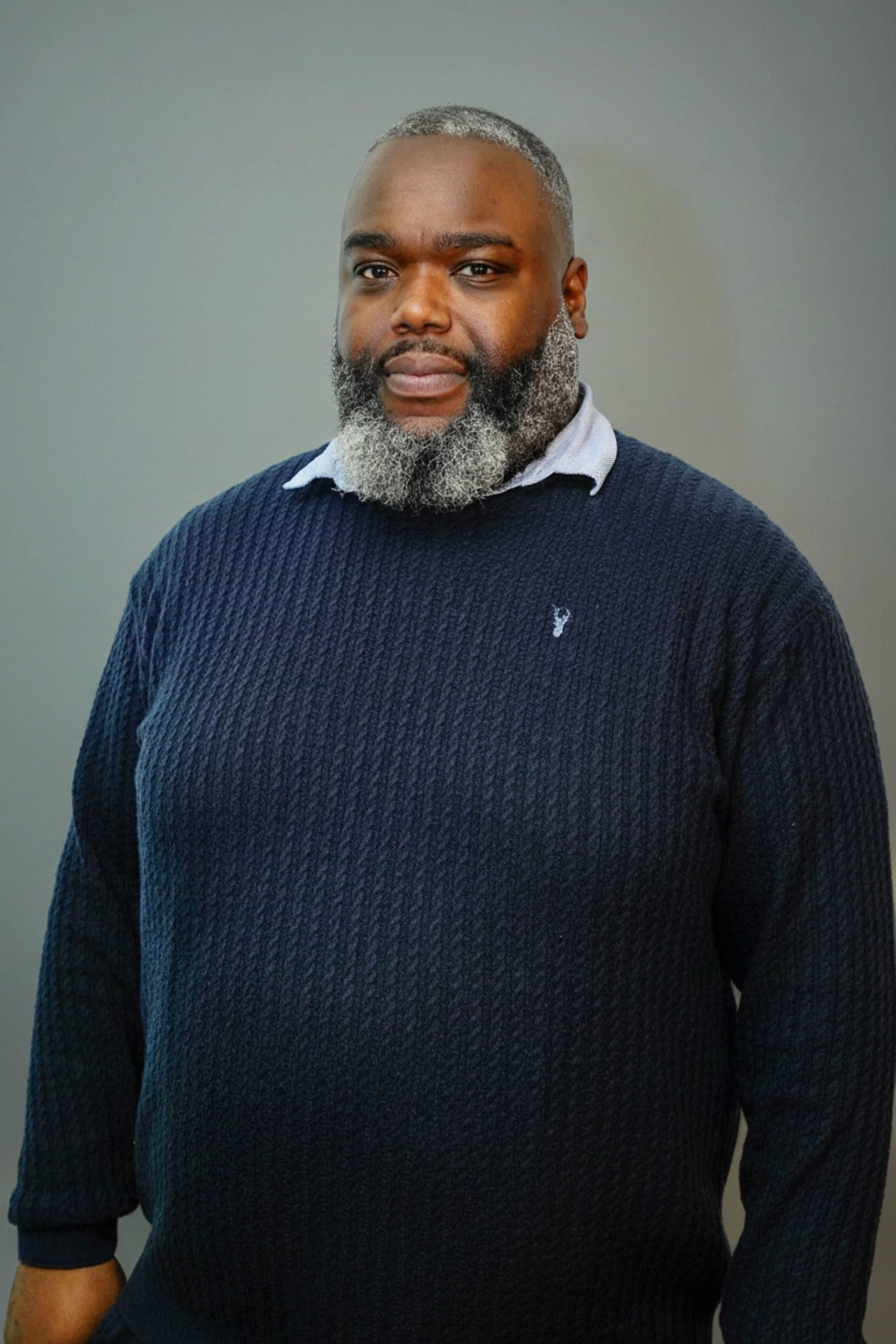 A close-up portrait of a smiling Black man with a well-groomed beard and short hairstyle, wearing a dark hoodie.