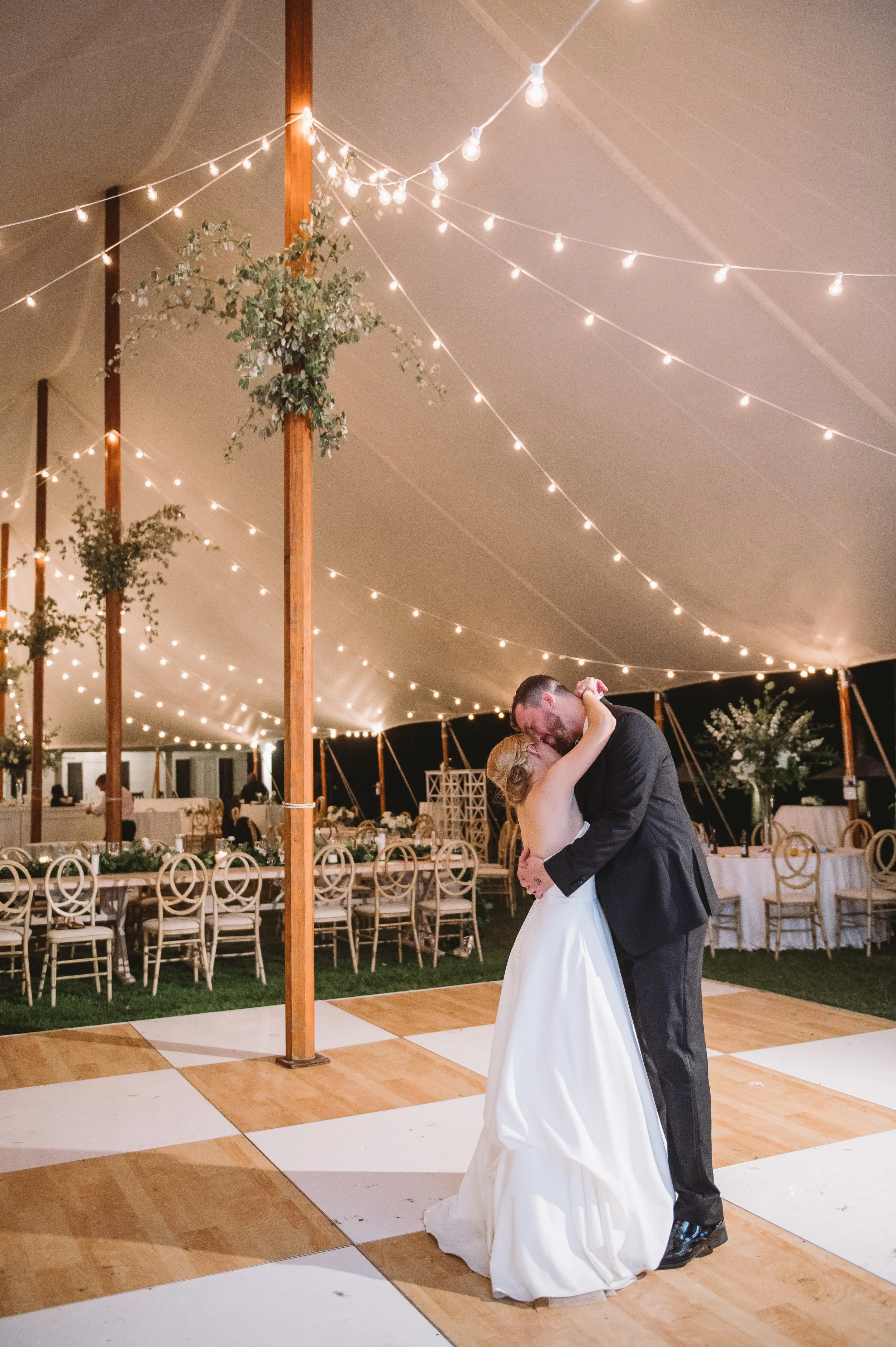Callie and John dance alone in the reception tent. It is night and there are string lights running up to the tent poles with bouquets on each pole.