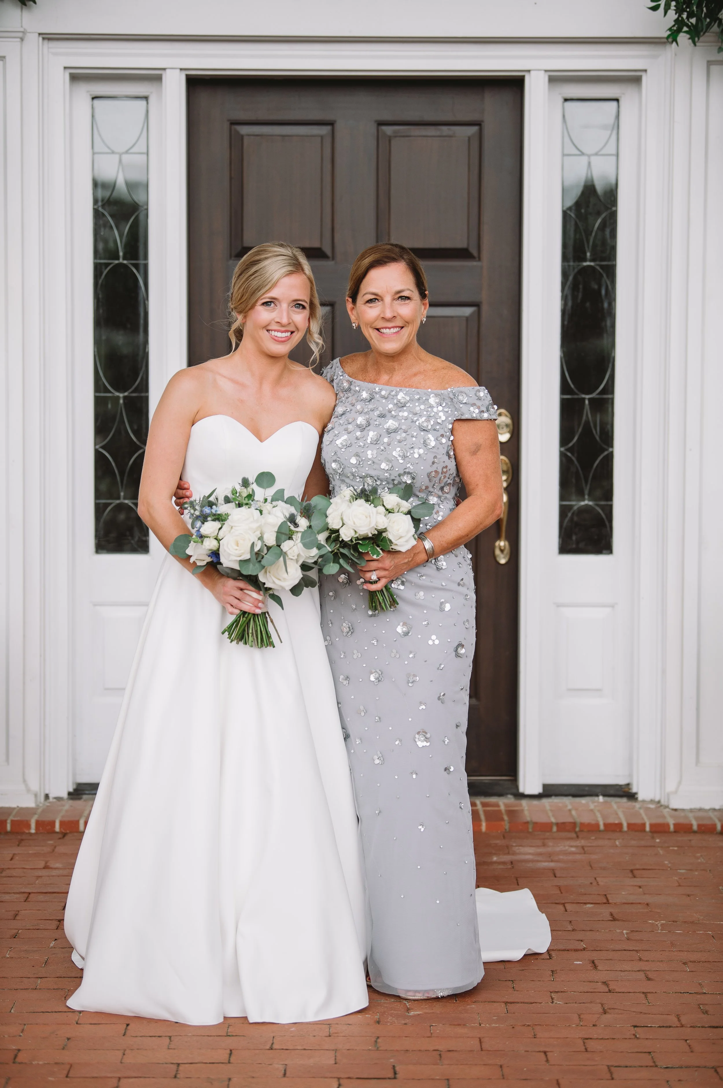 A traditional portrait of Callie and her mother smiling on the front porch. Both are holding bouquets and Callie's mother is wearing a light blue grey dress.