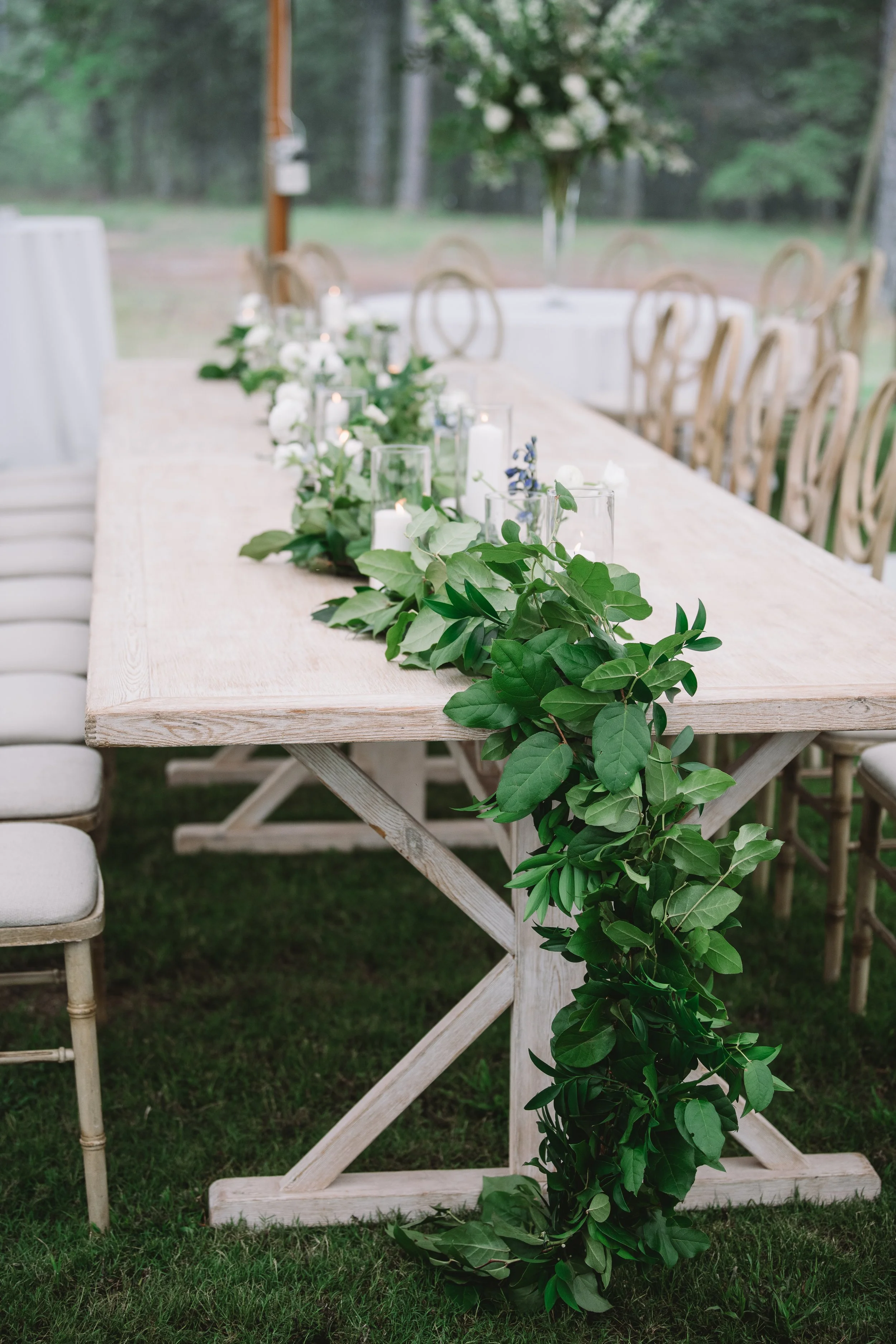 The party's reception table. There is a runner made up of greenery and candles running down the center.