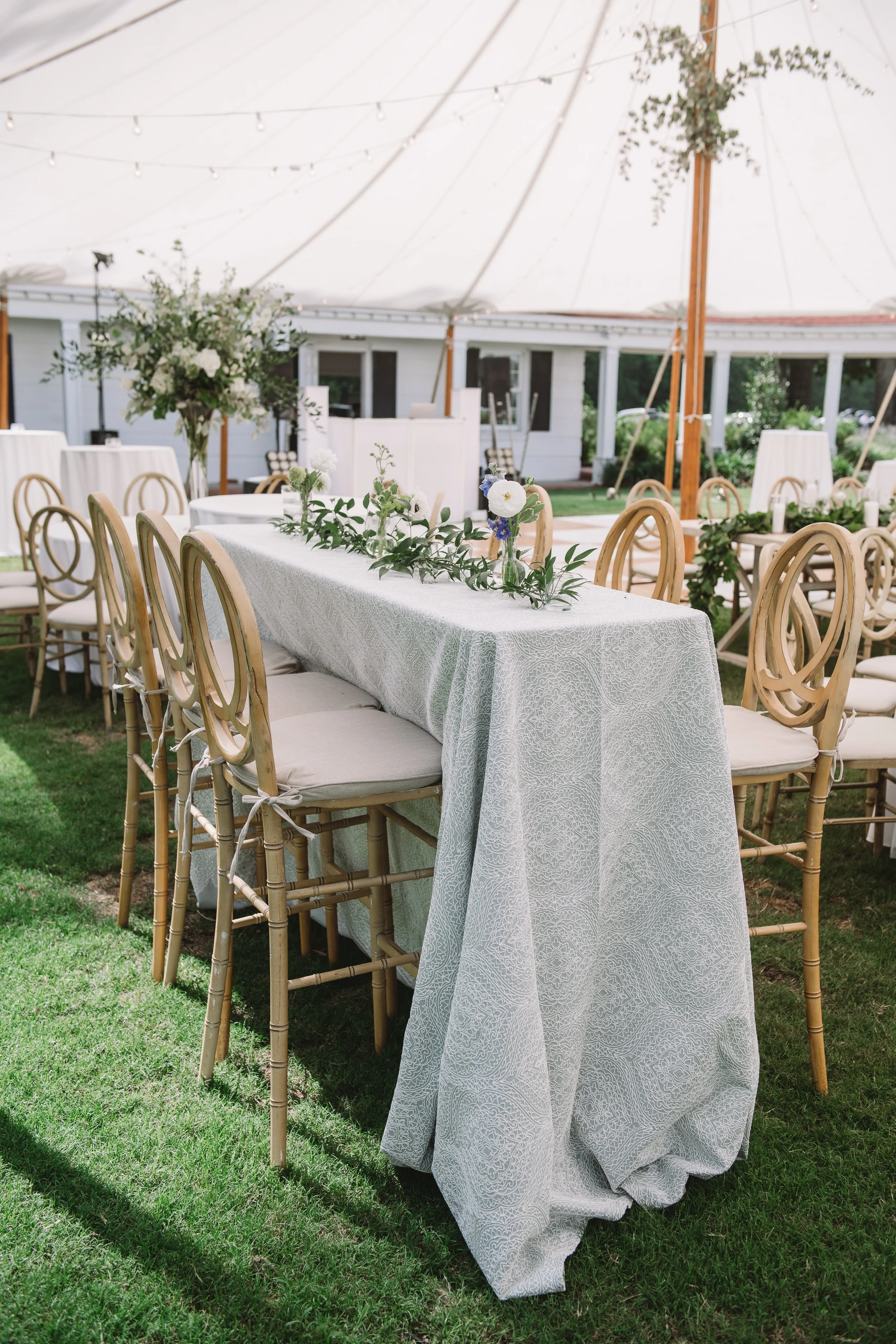 A high rise reception table with a table cloth and runner. The runner is made up of greenery and candles.