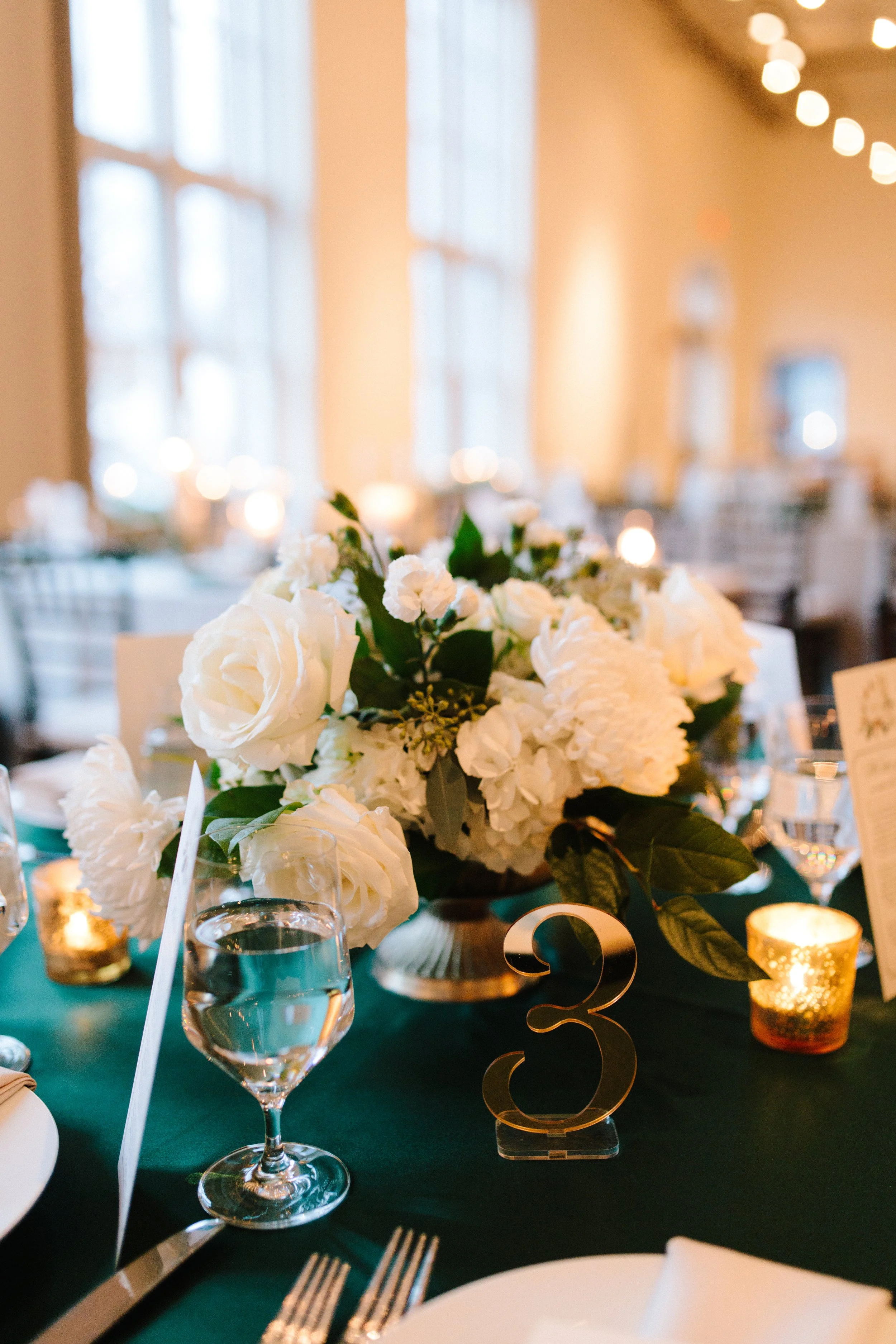 A closeup of a bouquet on one of the reception tables. The bouquet has white flowers including roses and greenery. 