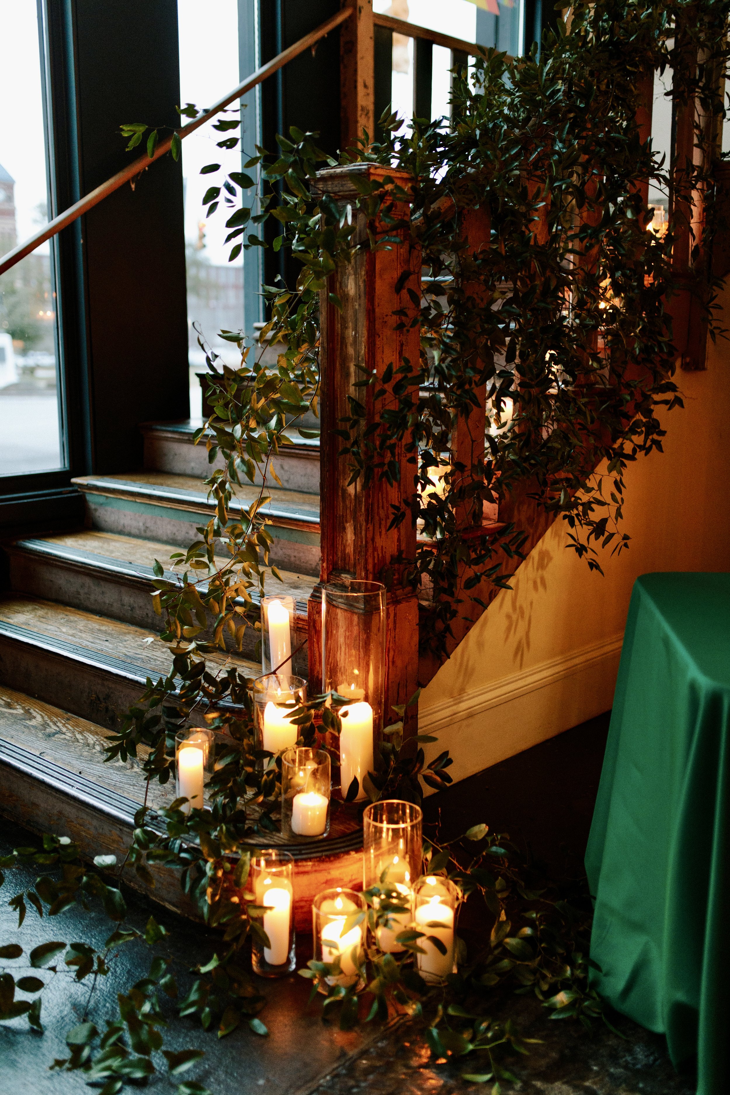 A wooden staircase adorned with green leafy vines and white candles.