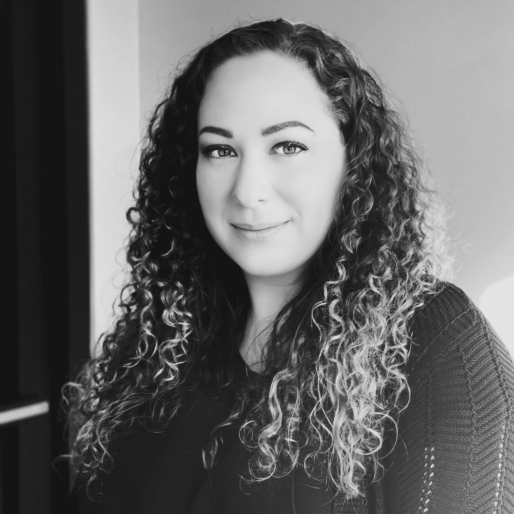 A woman with long, curly hair smiling in a black-and-white portrait.