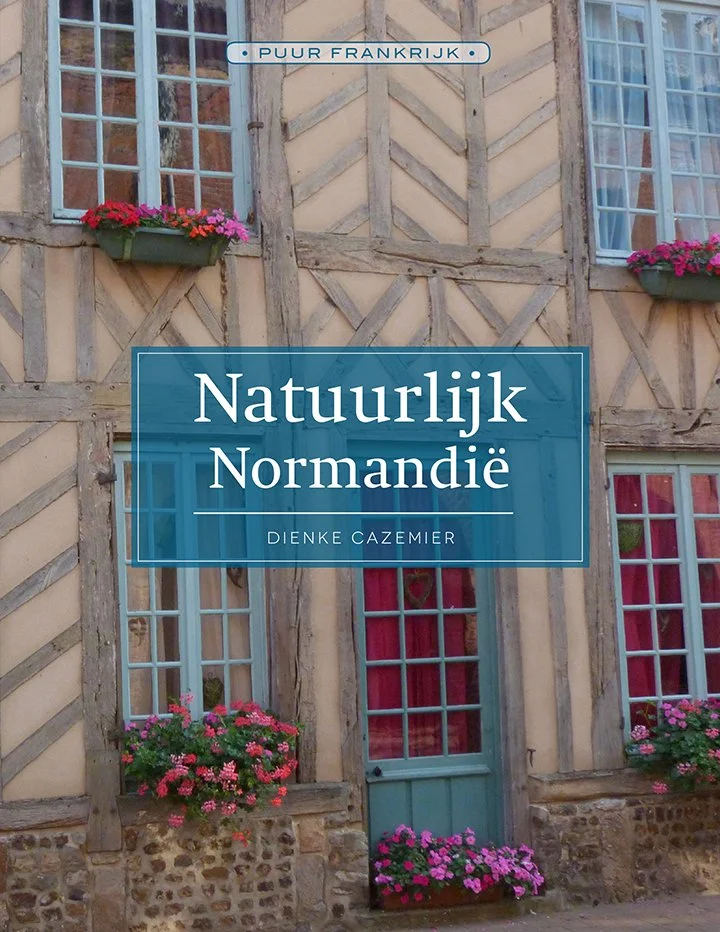 Boekcover met een foto van een traditioneel Normands huis met houten gevel en bloembakken met roze en paarse bloemen, titel 'Natuurlijk Normandië' door Dienne Cazemier.