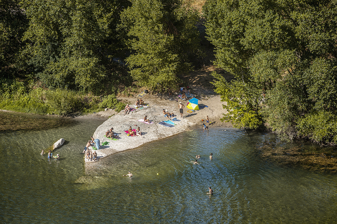 Mensen ontspannen op een klein strandje bij de rivier de Ardèche met zonneterrassen, baden in een rivier omgeven door groene bomen.