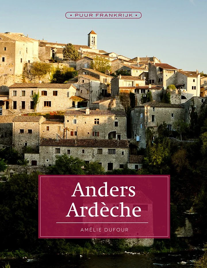Boekomslag van 'Anders Ardèche' door Amélie Dufour, met een foto van een heuvelachtig dorp met oude stenen huizen en een kerktorentje onder een heldere blauwe hemel.
