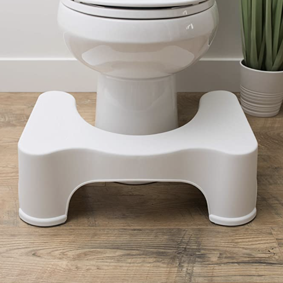 A white plastic step stool placed in front of a toilet with a potted plant nearby on a wooden floor.