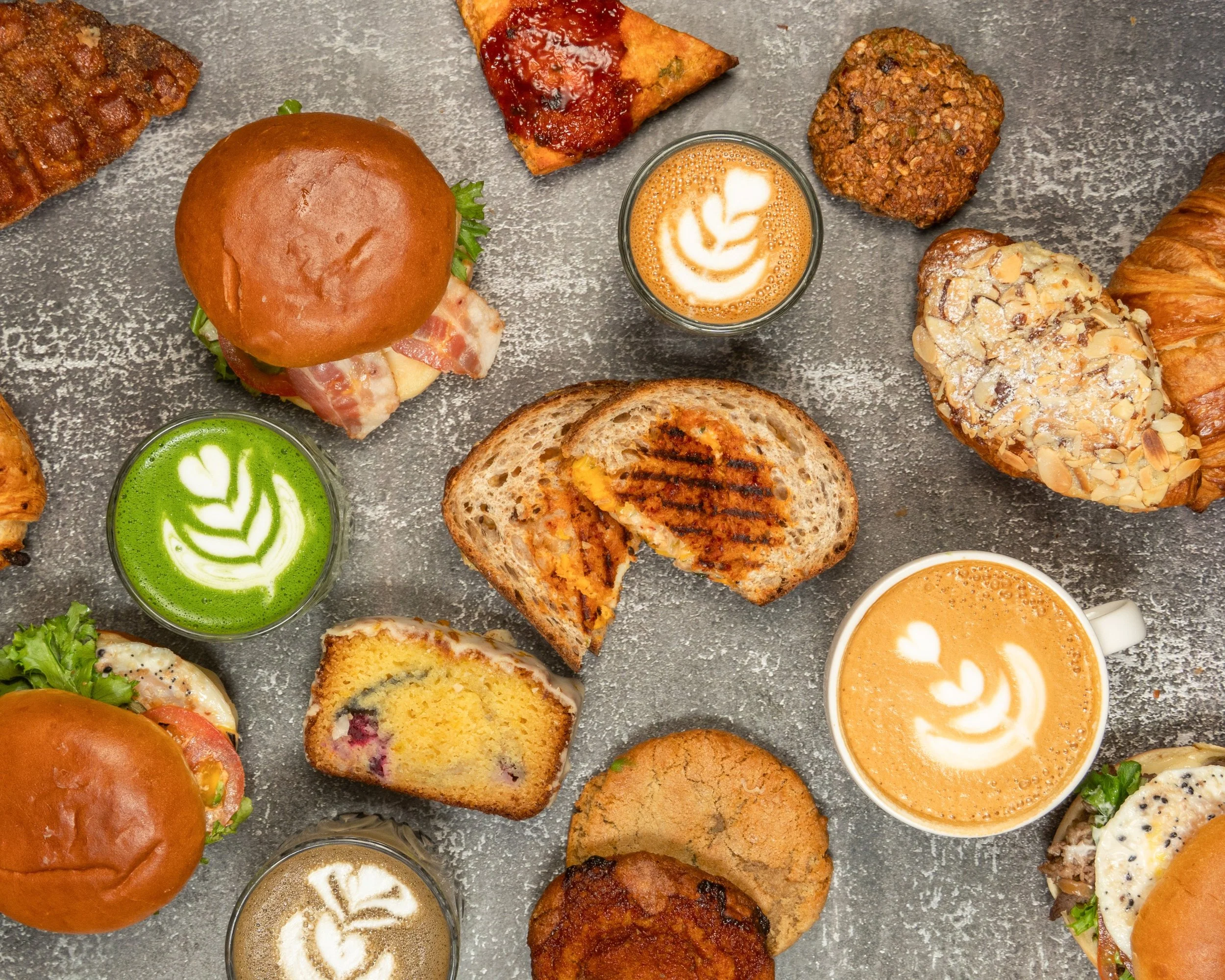 A baked pastry topped with caramelized fruit and sesame seeds on a white plate, with other pastries blurred in the background.