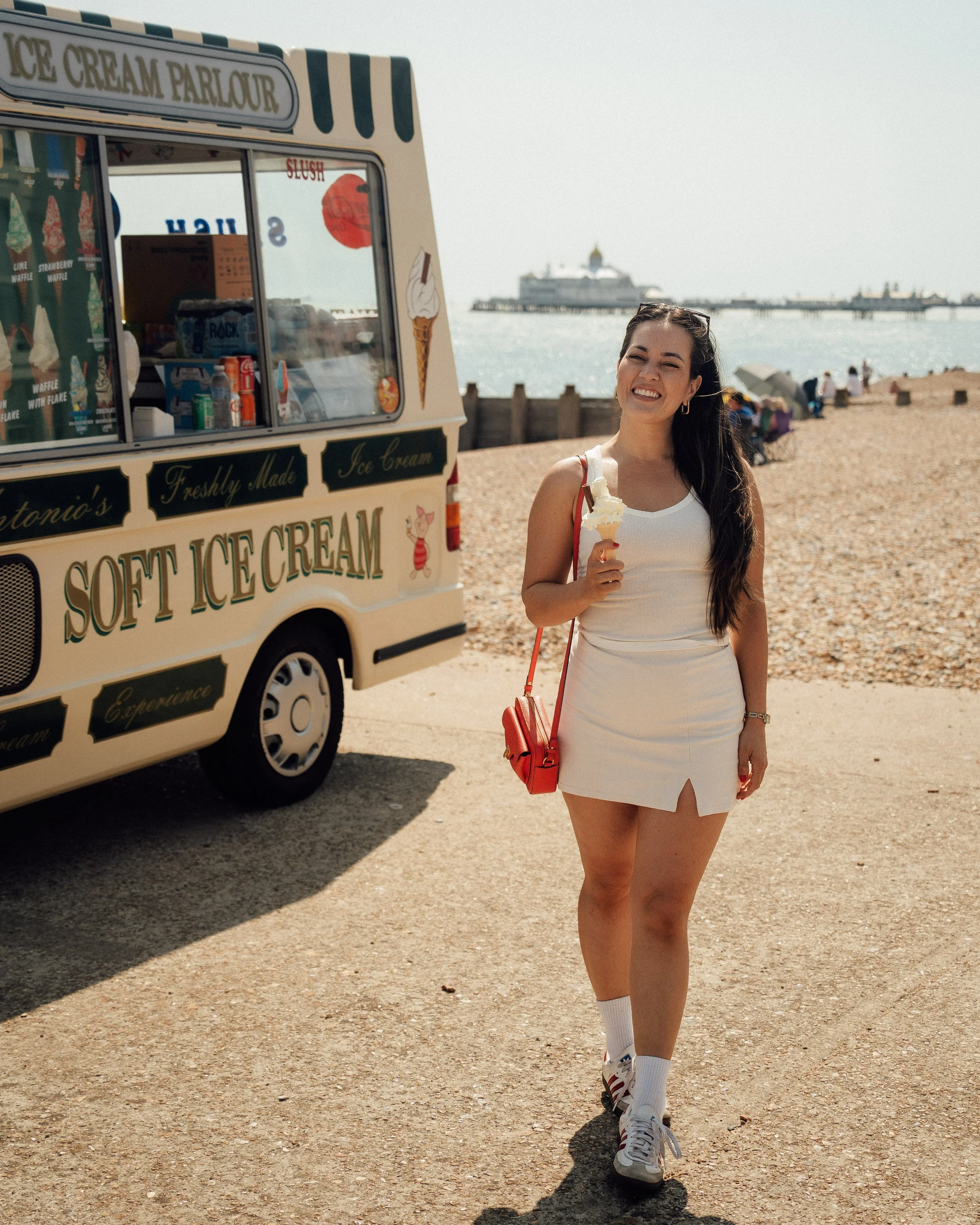 woman holding an ice cream cone in front of an ice cream van on the pebble beach in Eastbourne, England.