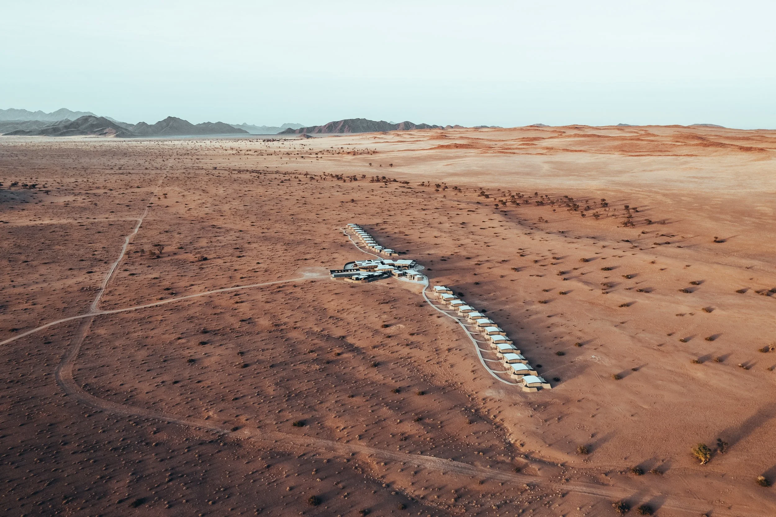 Aerial drone view of The Desert Grace lodge bungalows stretching across the vast red sand landscape of Gondwana Namib Park in Namibia
