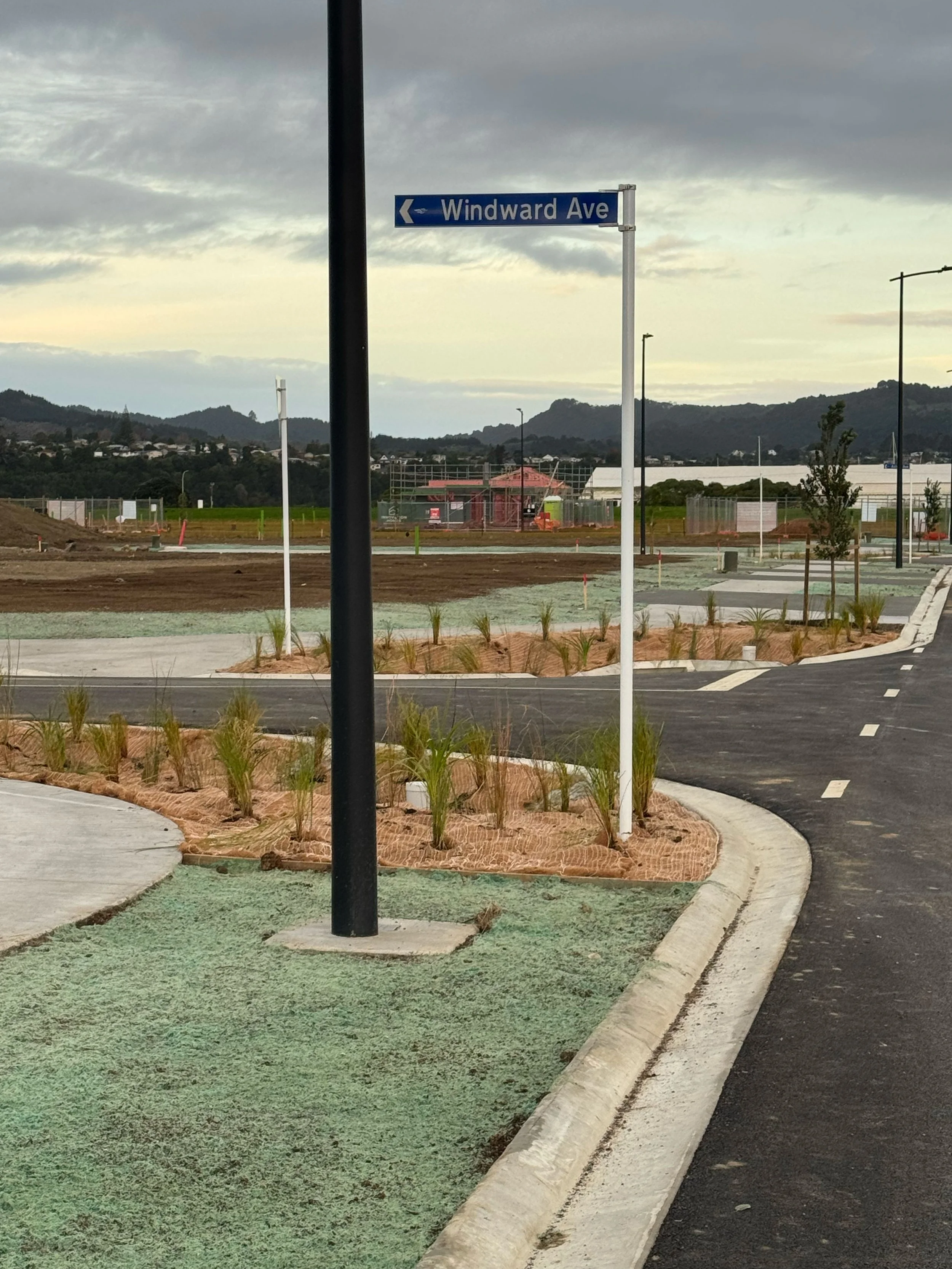 Street sign indicating Windward Avenue in a suburban or developing area with green landscaping, mountains in the distance, and overcast sky.