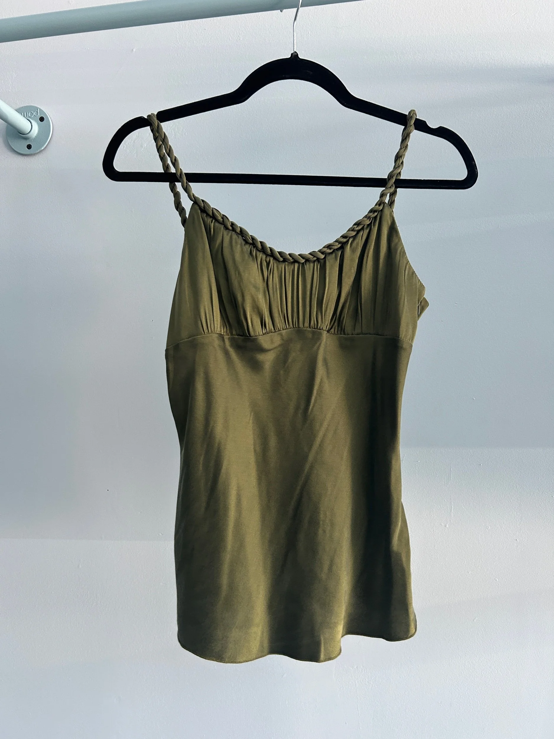 A gold satin dress with braided straps hanging on a black hanger from a white closet rod against a plain white wall.
