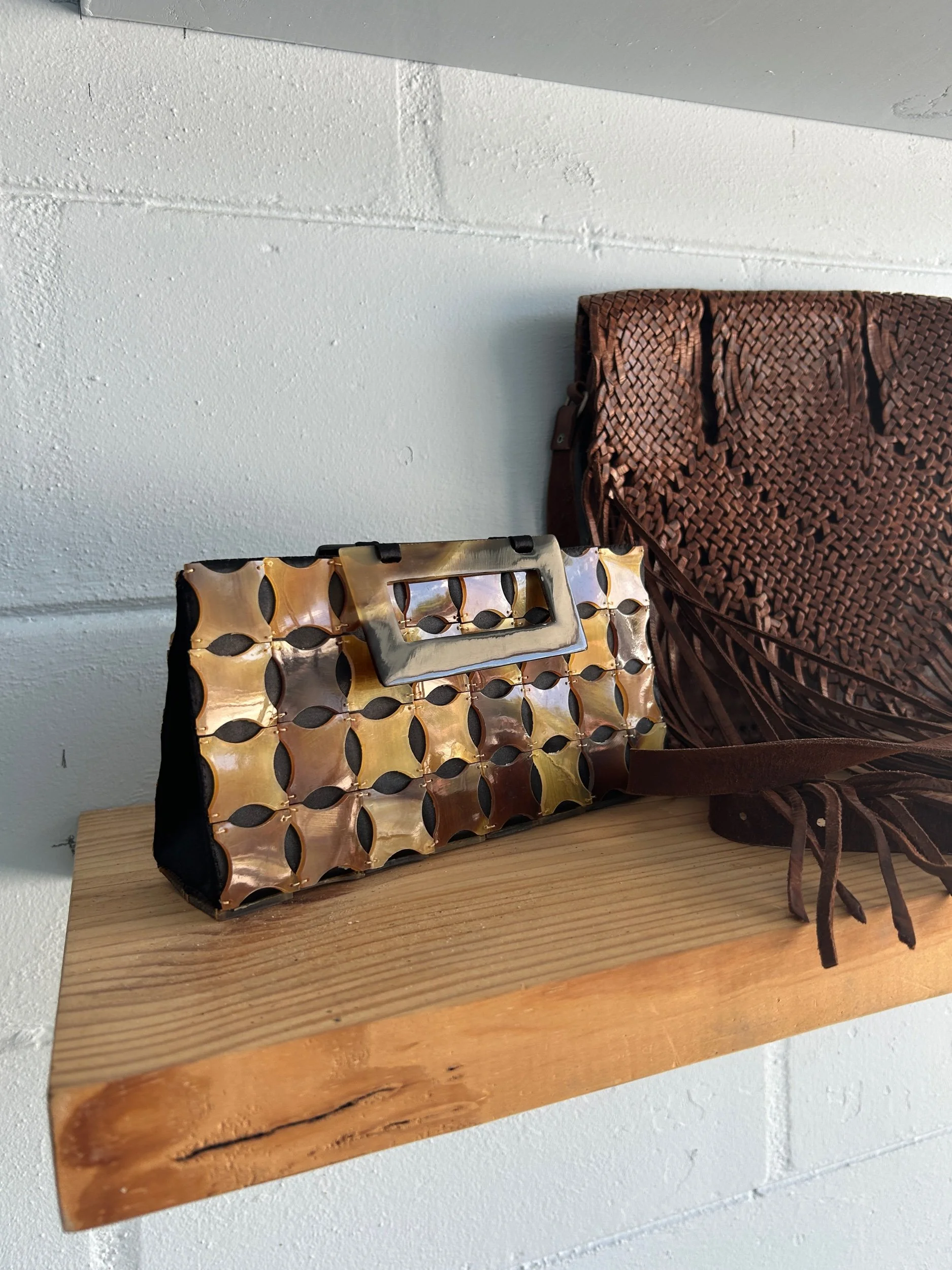 A vintage handbag with a metal handle and a lattice pattern in shades of brown and gold, placed on a wooden surface next to a clutch with a similar lattice design.