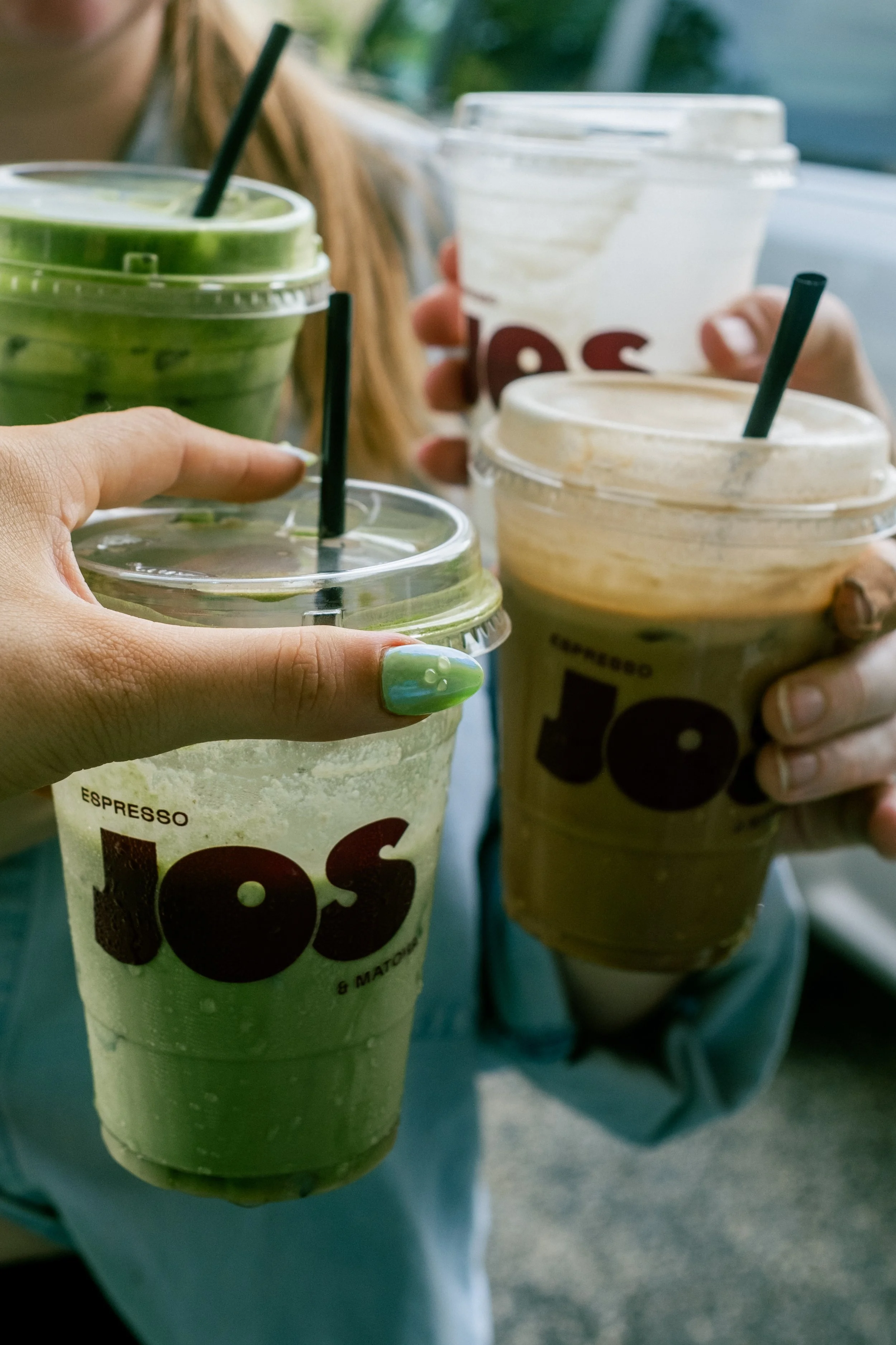 Close-up of multiple people holding cold coffee beverages in plastic cups with straws, some with green lids, in a casual setting.