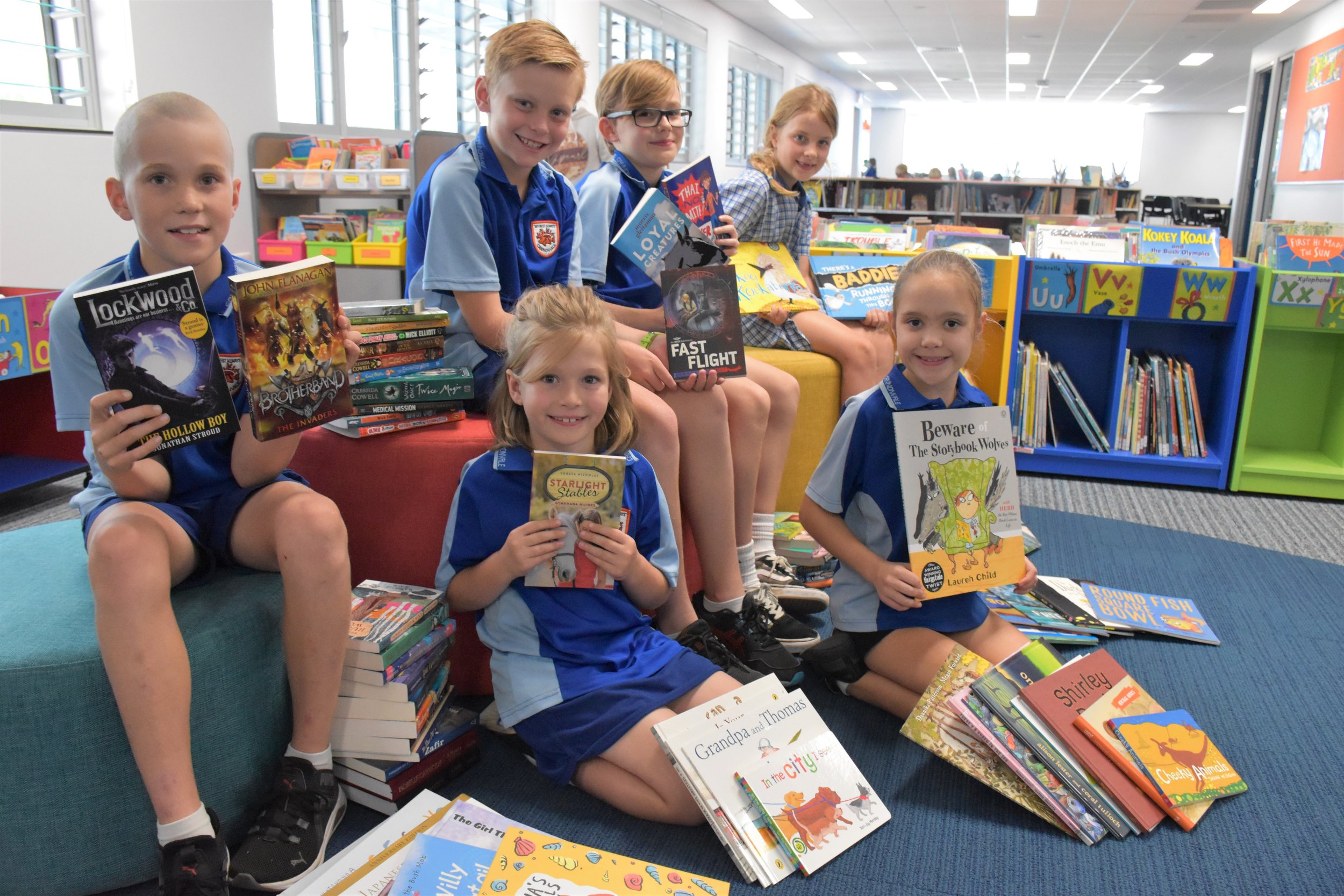 Children sitting in a library holding books and surrounded by stacks of books.